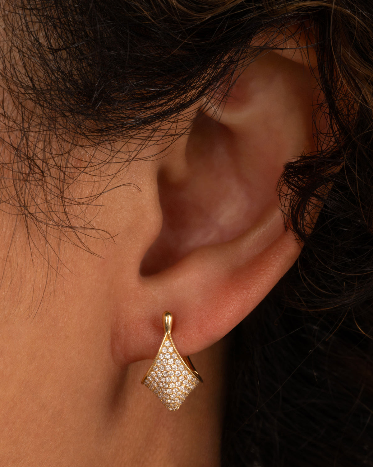 Artemer huggie hoop earring in yellow gold worn on an ear, an angular kite-shaped front covered in pave diamonds