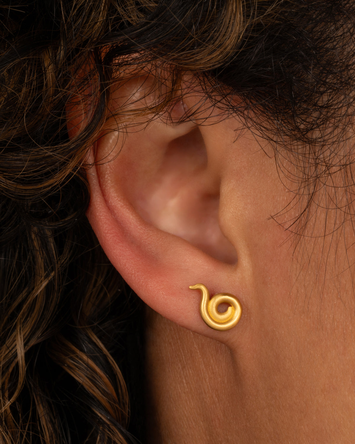 Lori Leven coiled stud earring in matte yellow gold worn on an ear, a gold coil that spirals up into a point