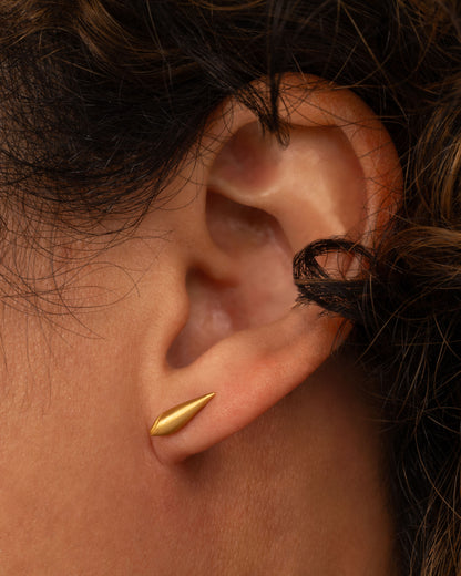 Lori Leven stud earring in matte yellow gold worn on an ear, a long ribbed gold shape like a closed shell