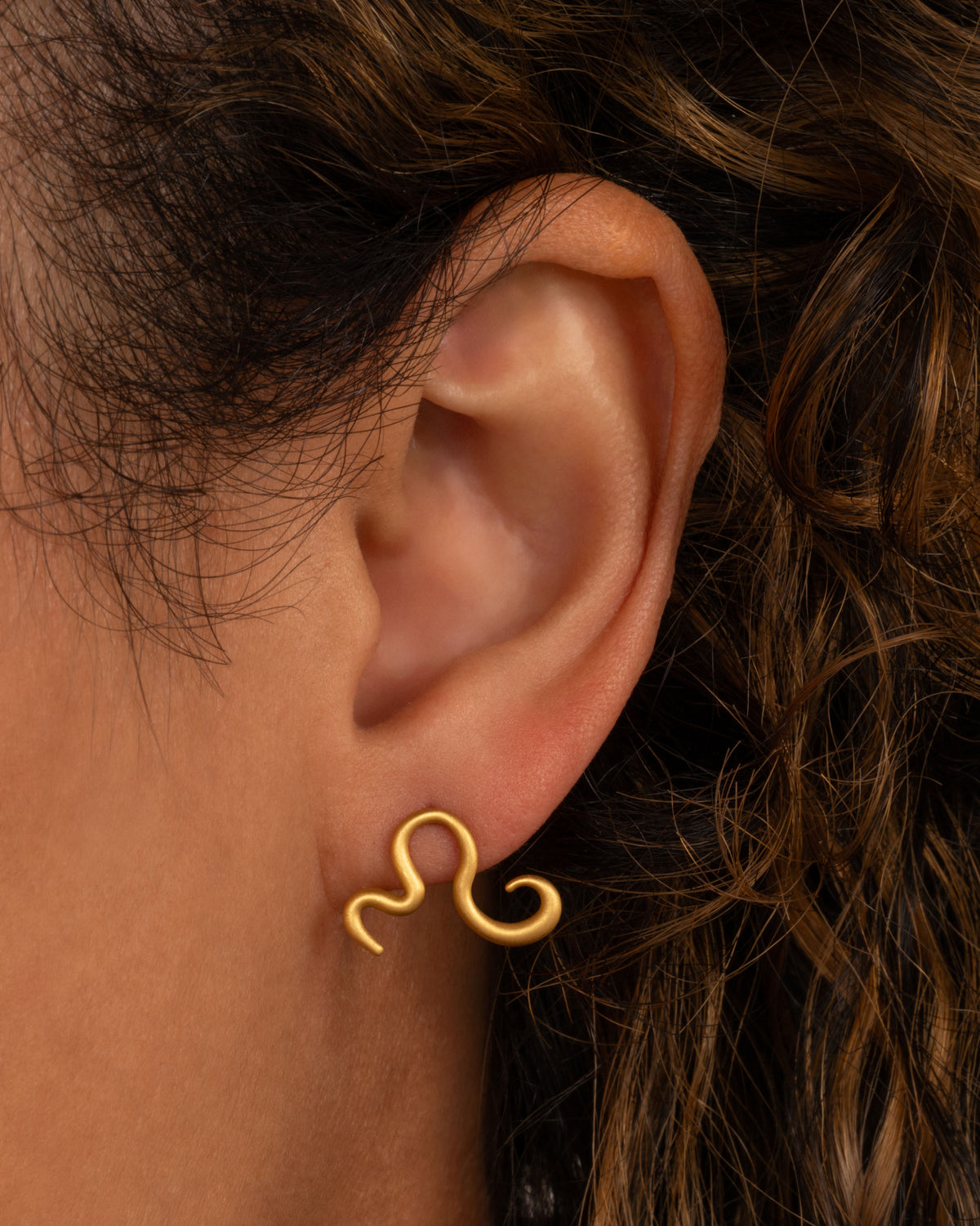 Lori Leven snake earring in 22k matte yellow gold worn on an ear, a gold stud curving like a snake