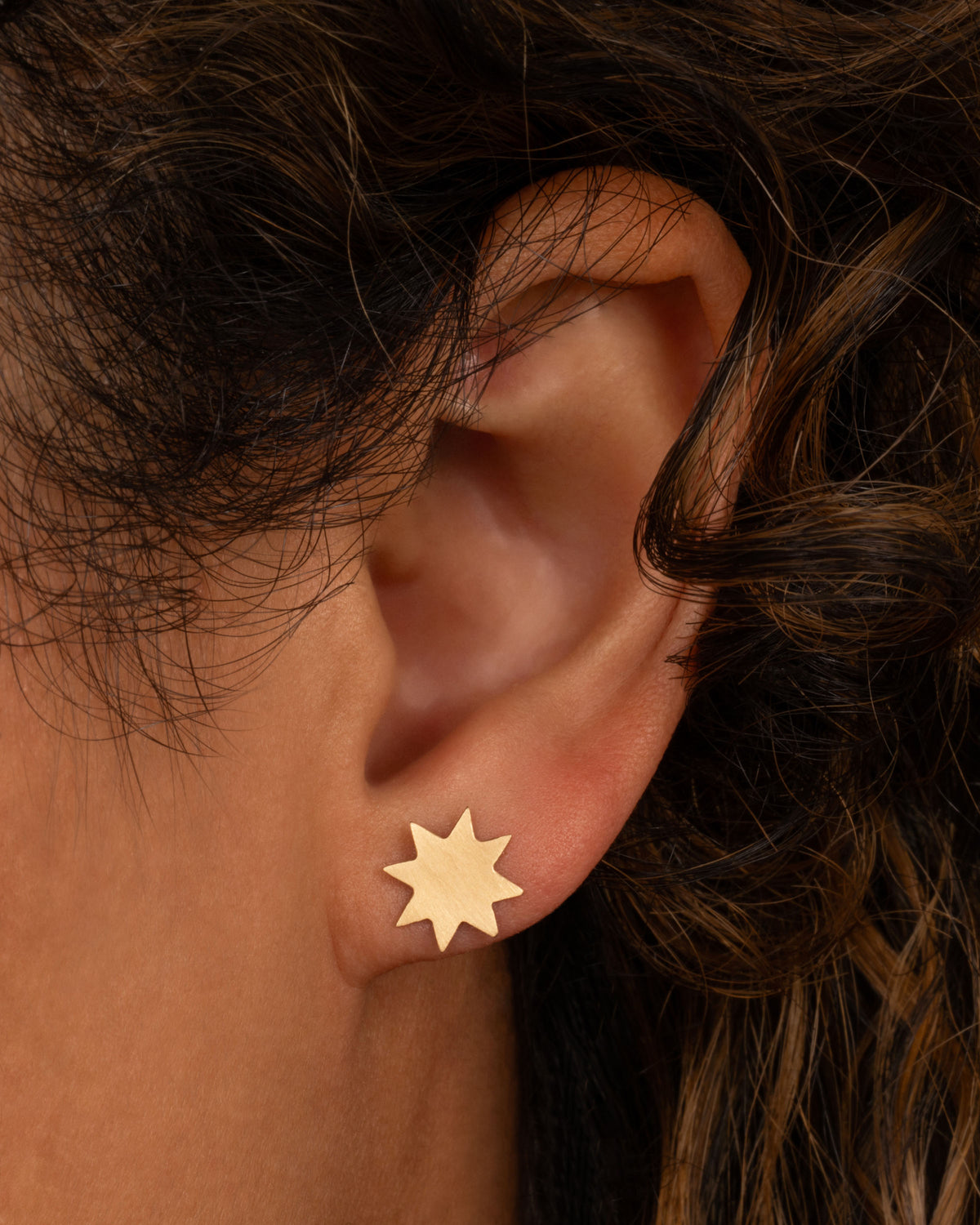 Lori Leven eight-point star stud earring in yellow gold worn on an ear, a flat brushed gold star