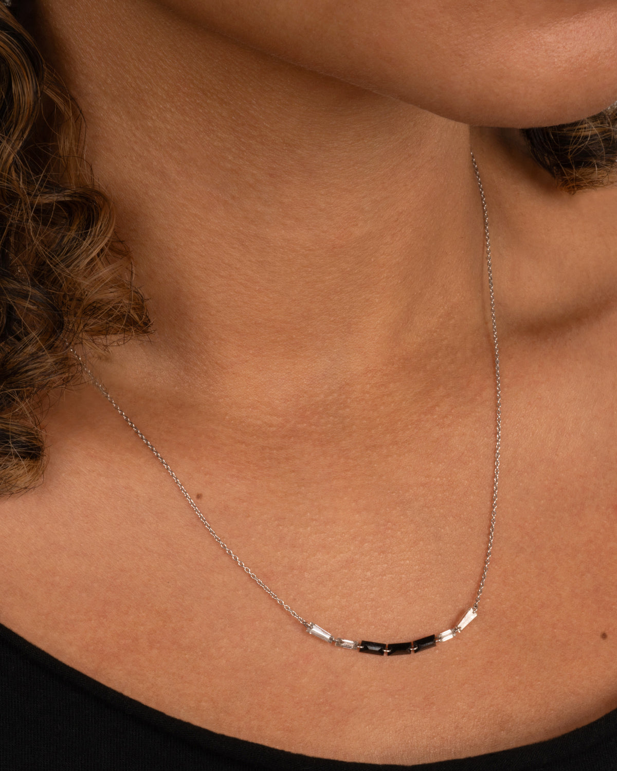 A white gold cable chain with black and white baguette diamonds connected by platinum jump rings, shown on a person.