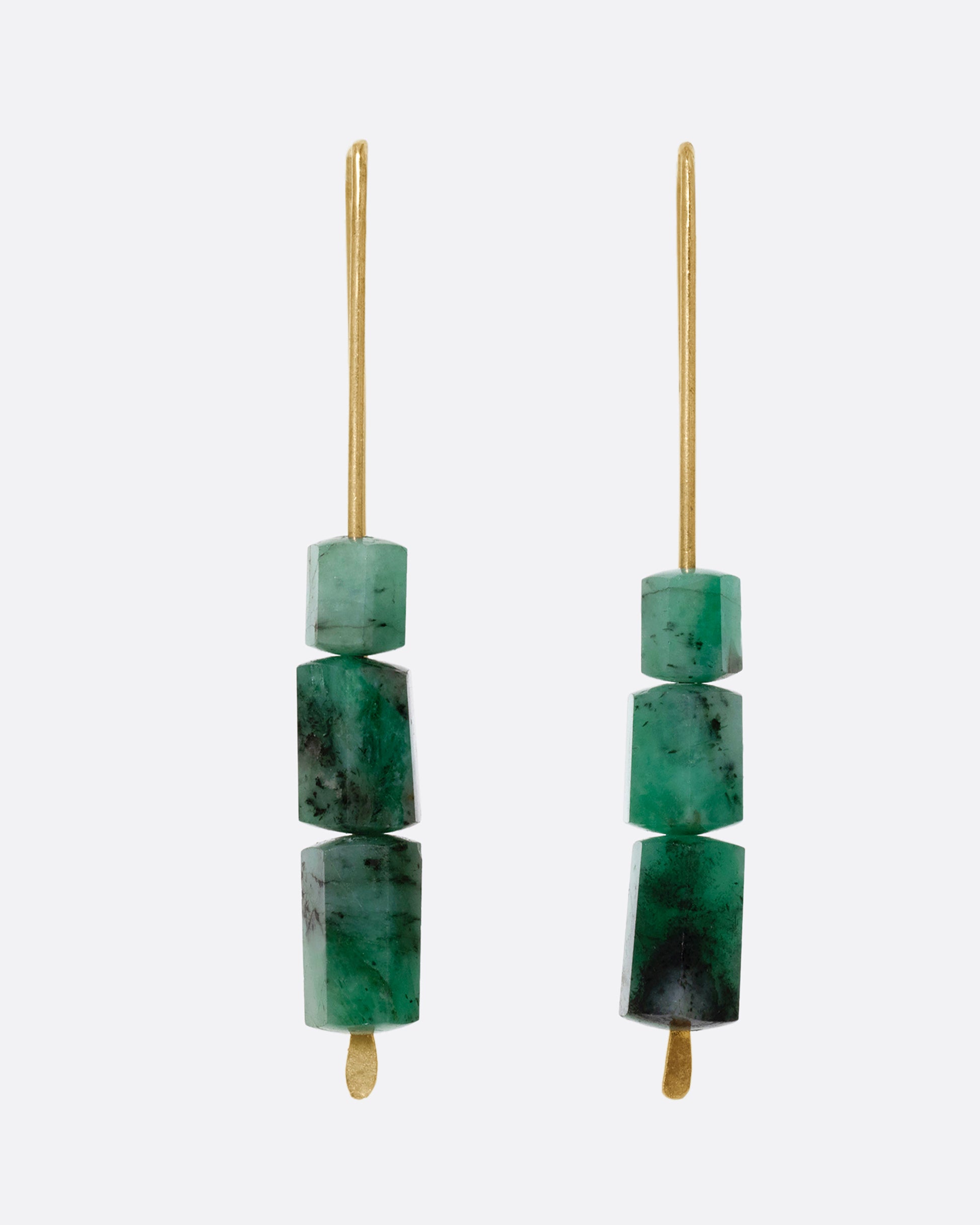 A pair of yellow gold hook earrings with three stacked freeform emeralds. Shown from the front.  