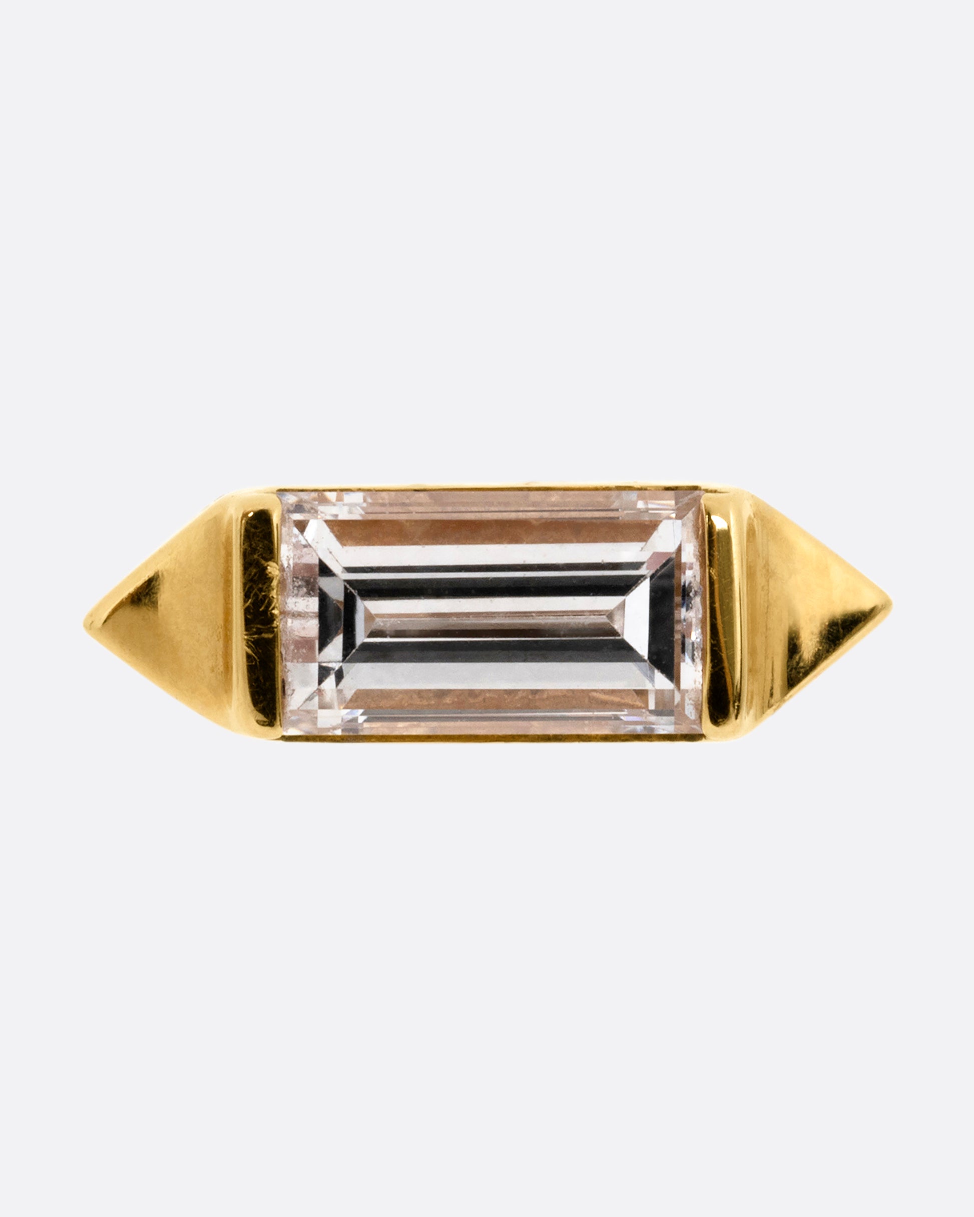 A yellow gold stud earring with a baguette diamond, bookended with points. Shown from the front.