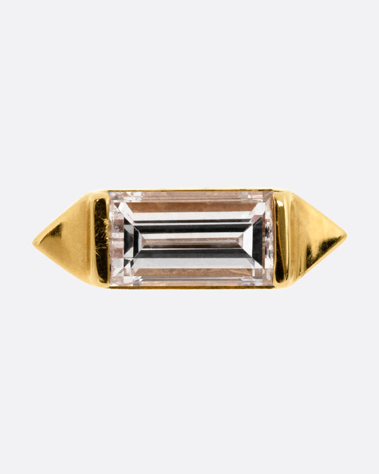 A yellow gold stud earring with a baguette diamond, bookended with points. Shown from the front.