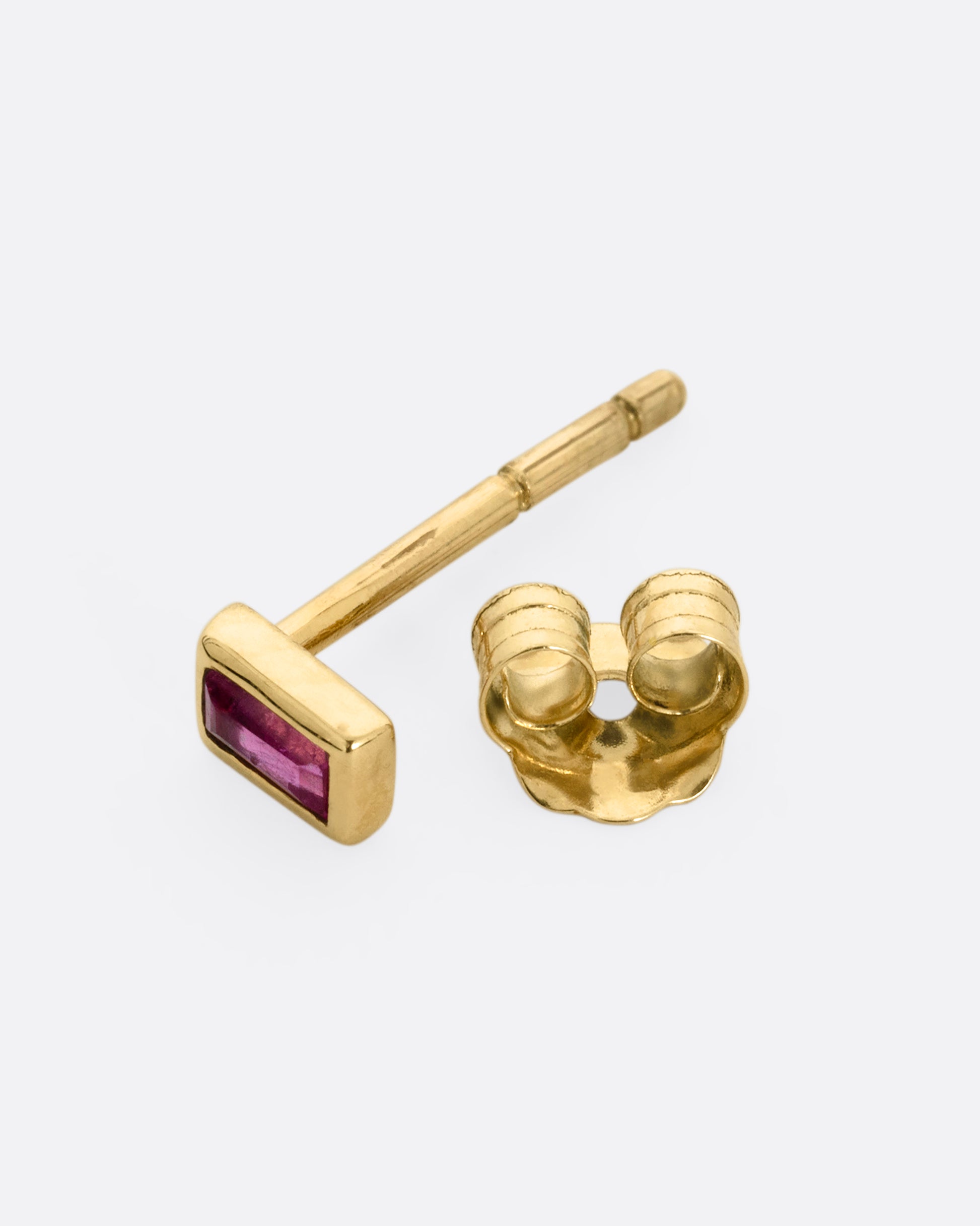 A yellow gold stud earring with a baguette cut ruby, shown open on its side.