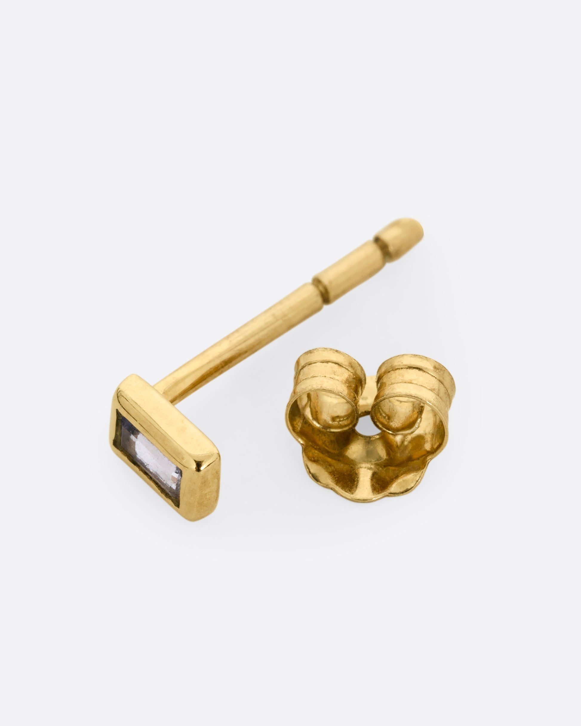A yellow gold stud earring with a baguette cut ruby, shown open on its side.