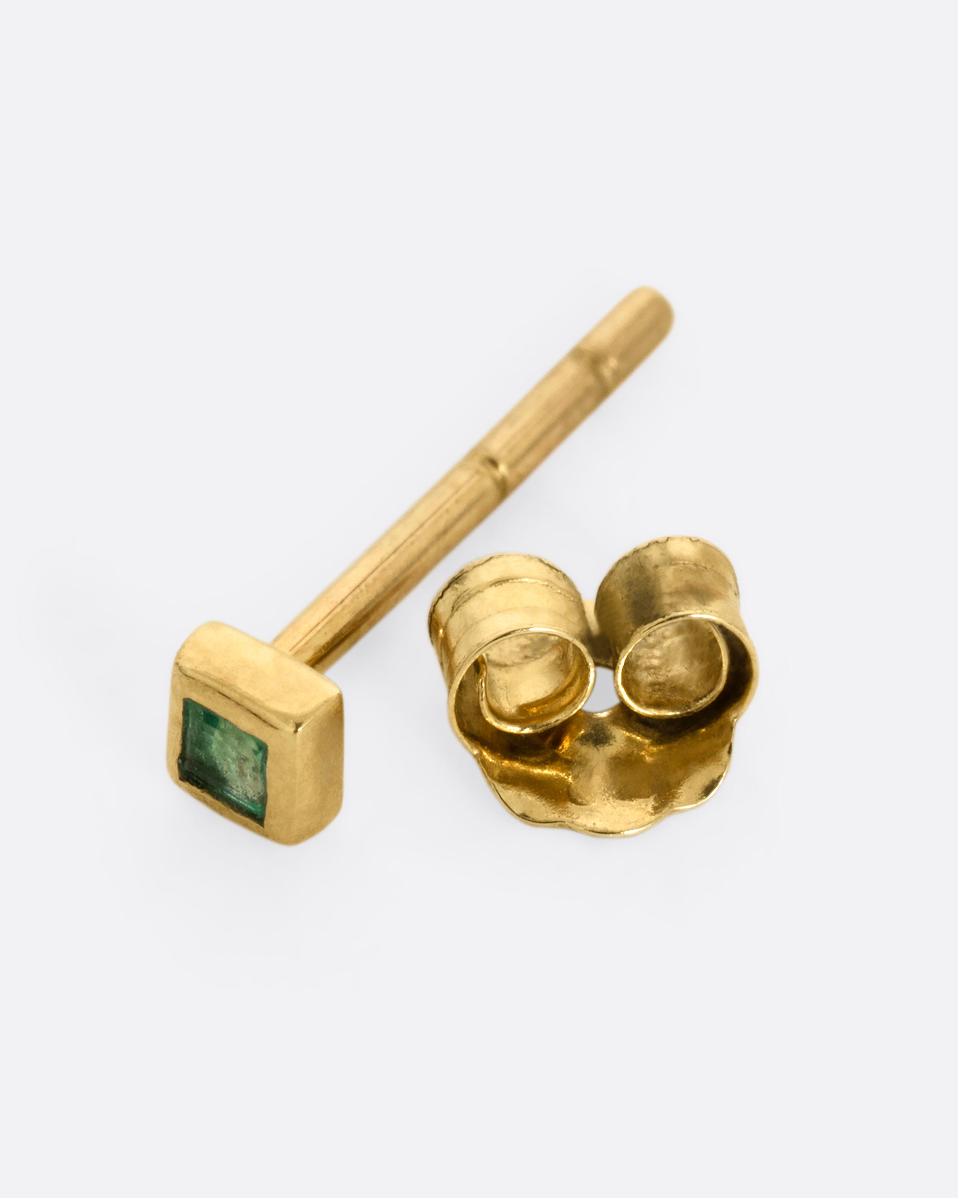A yellow gold stud earring with a princess cut emerald, shown open on its side.