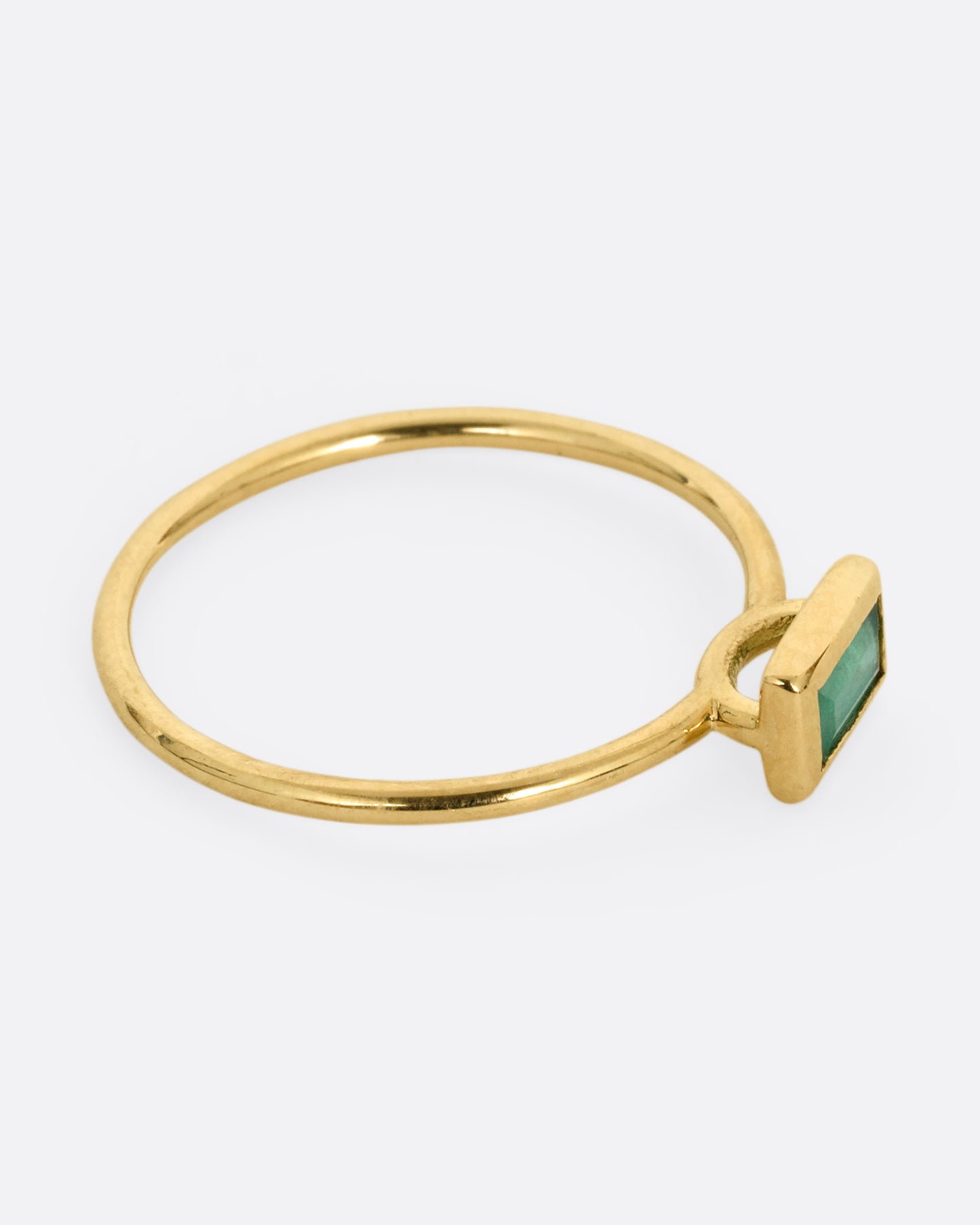 A yellow gold ring with an emerald baguette, shown from the side.