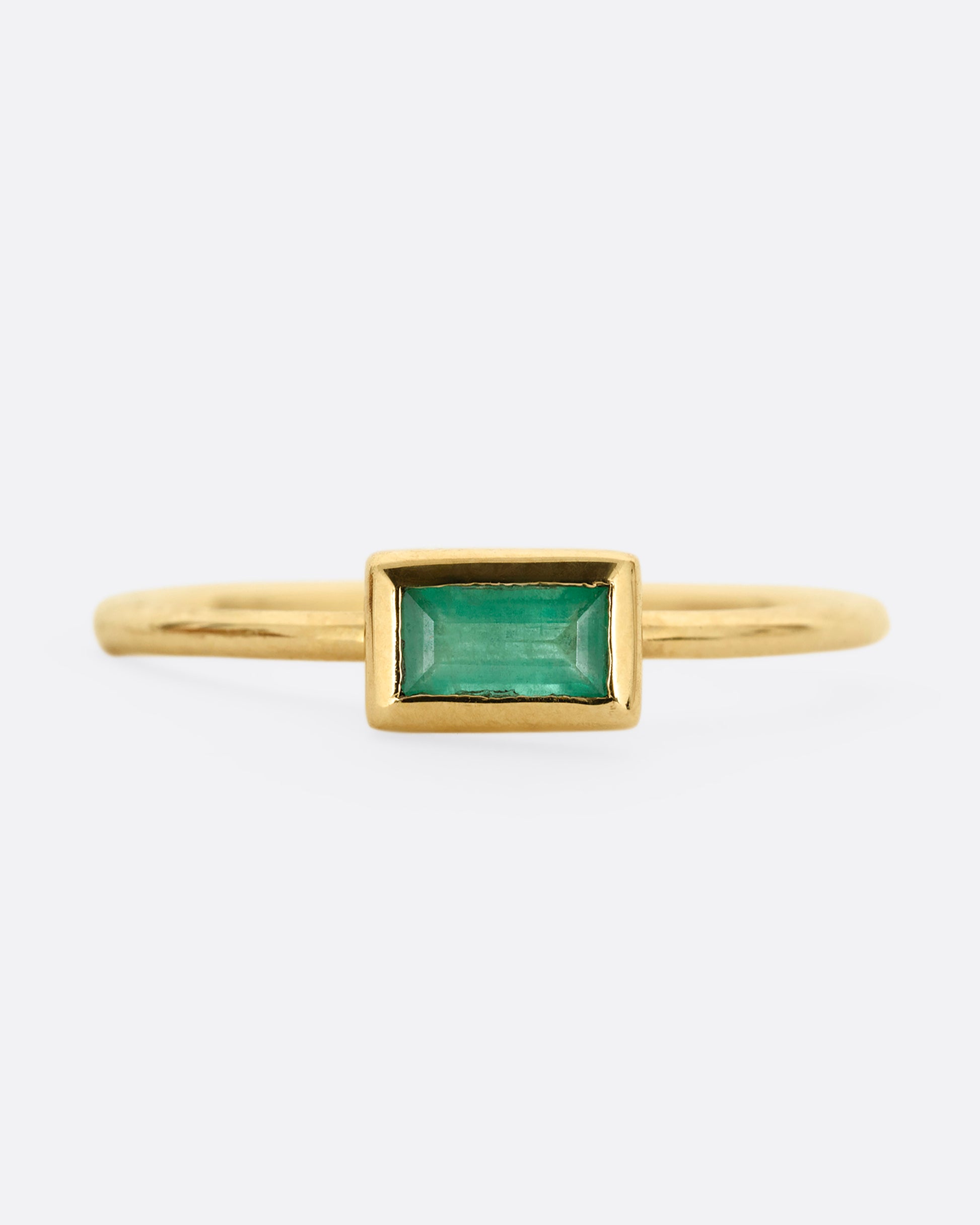 A yellow gold ring with an emerald baguette, shown from the front.