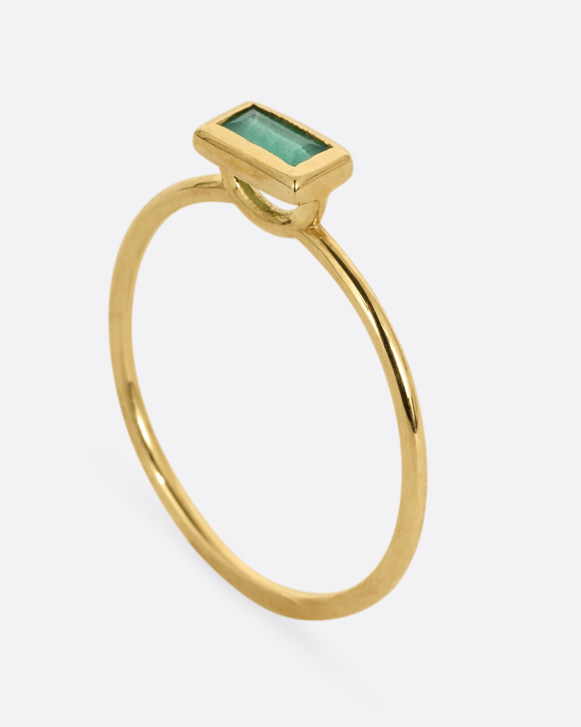 A yellow gold ring with an emerald baguette, shown from the side standing up.