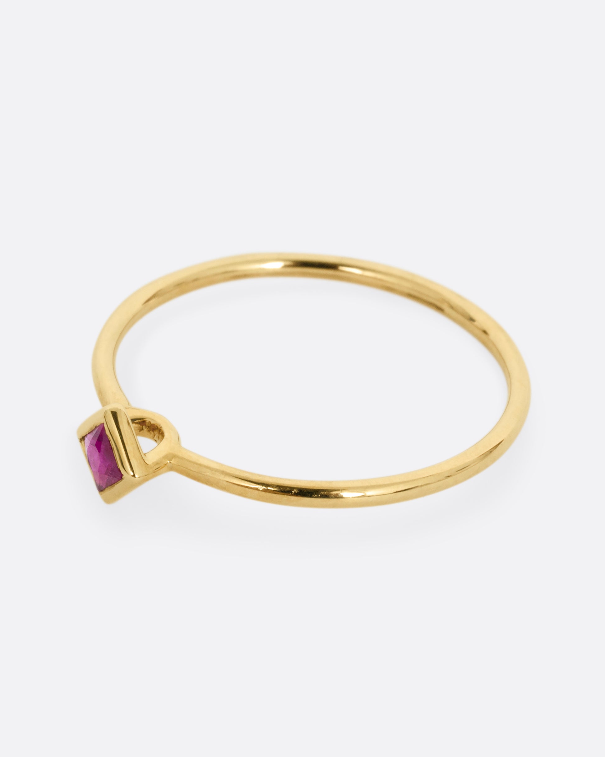 A yellow gold ring with a princess cut ruby, shown from the side.