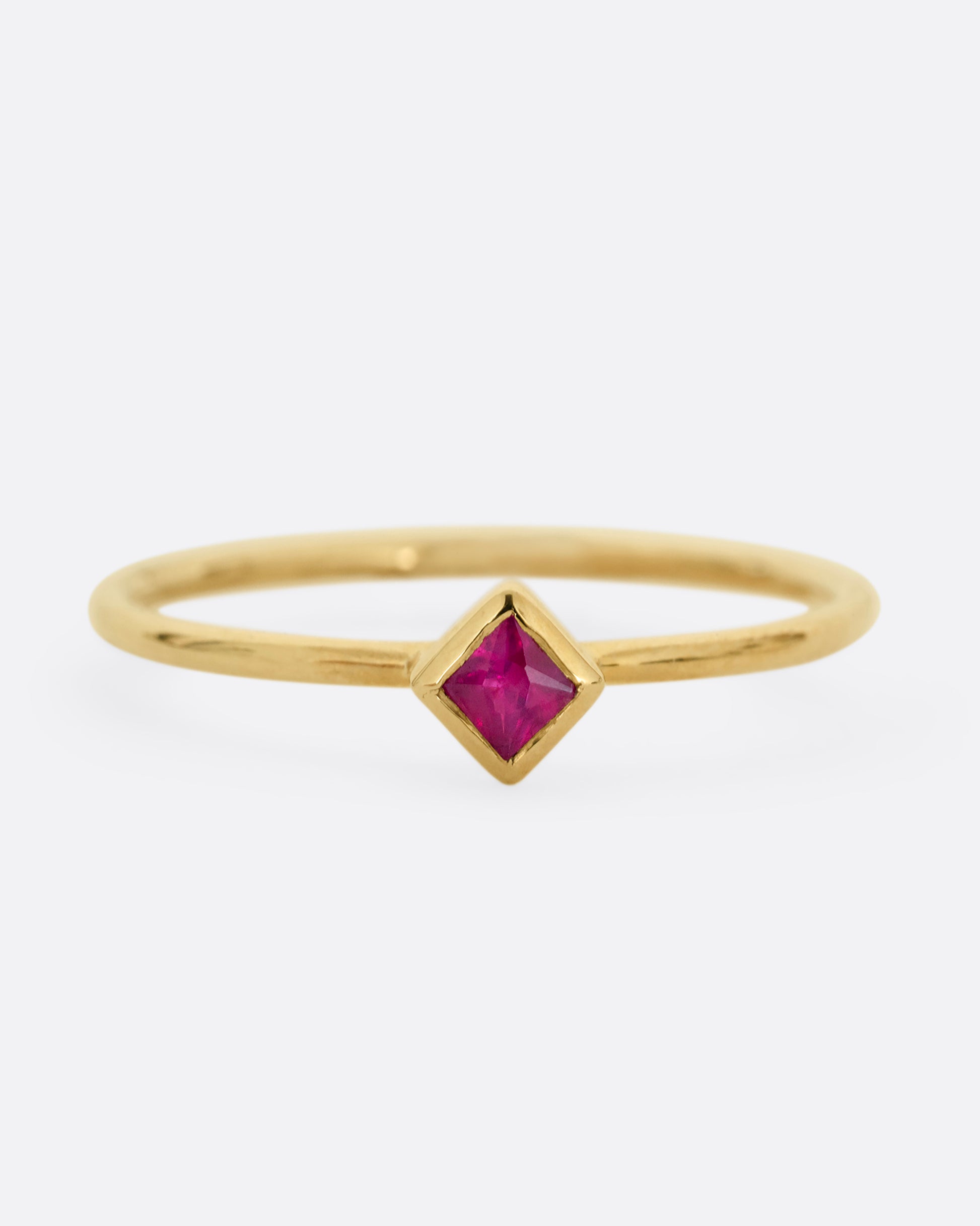 A yellow gold ring with a princess cut ruby, shown from the front.