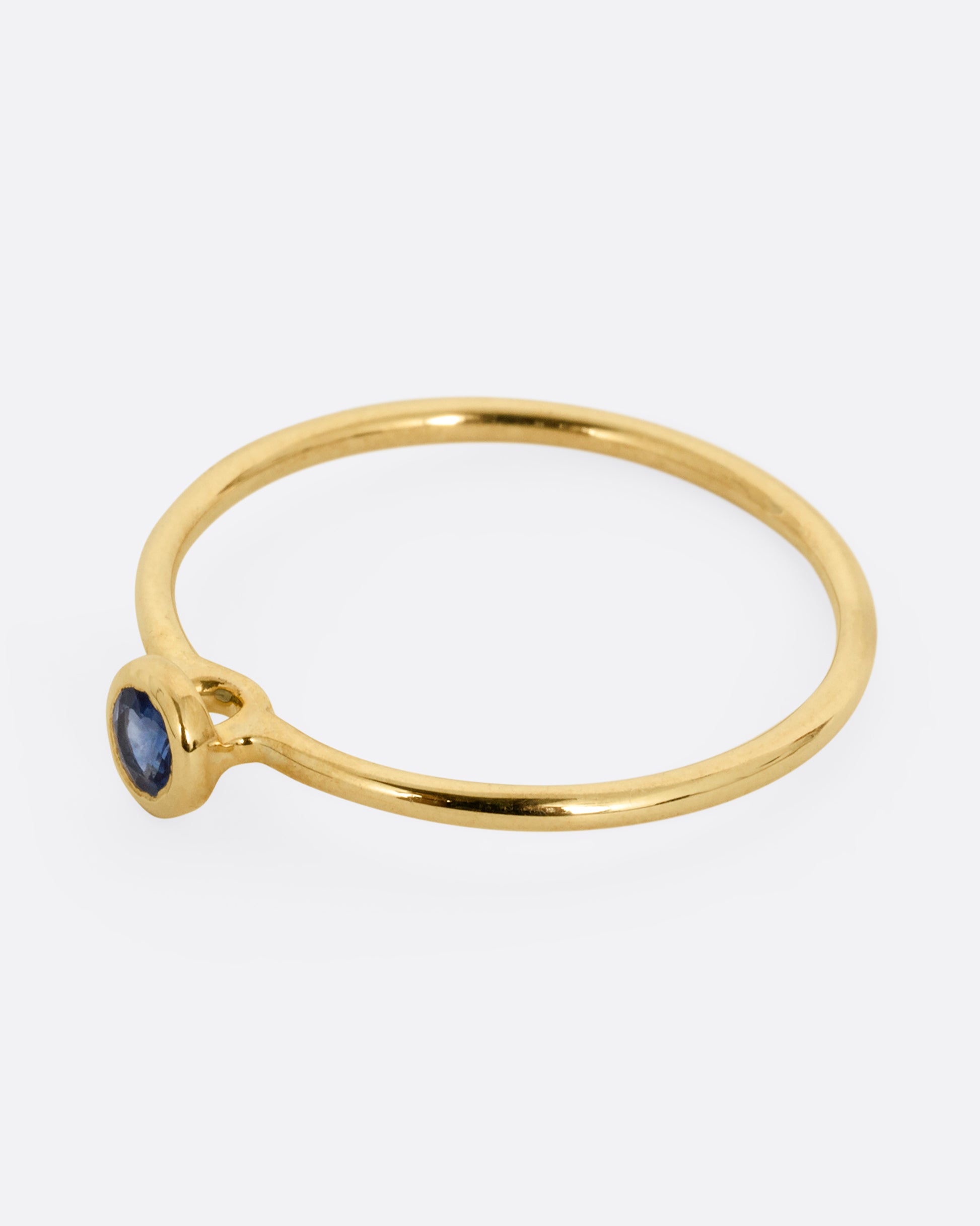 A yellow gold ring with a round sapphire, shown from the side.
