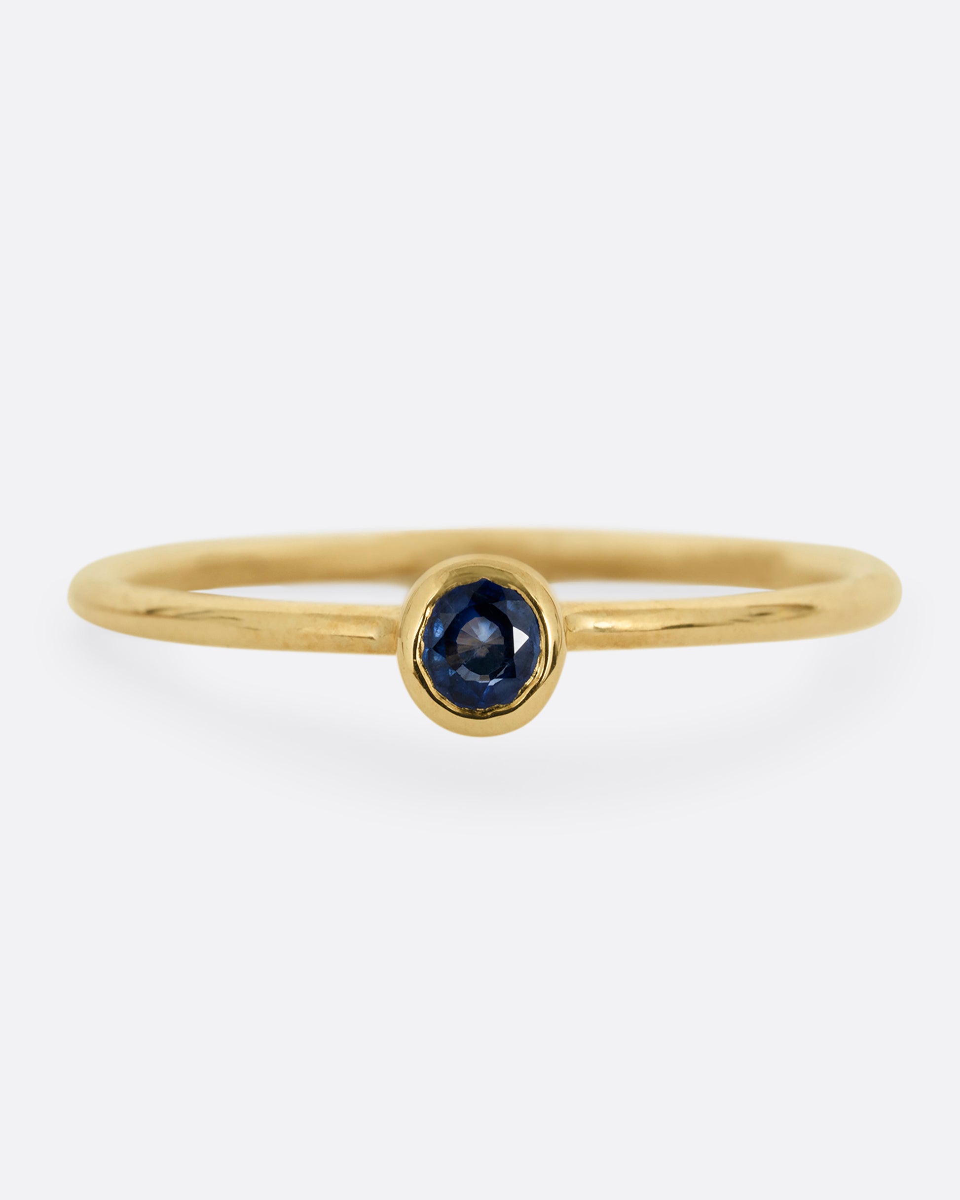 A yellow gold ring with a round sapphire, shown from the front.