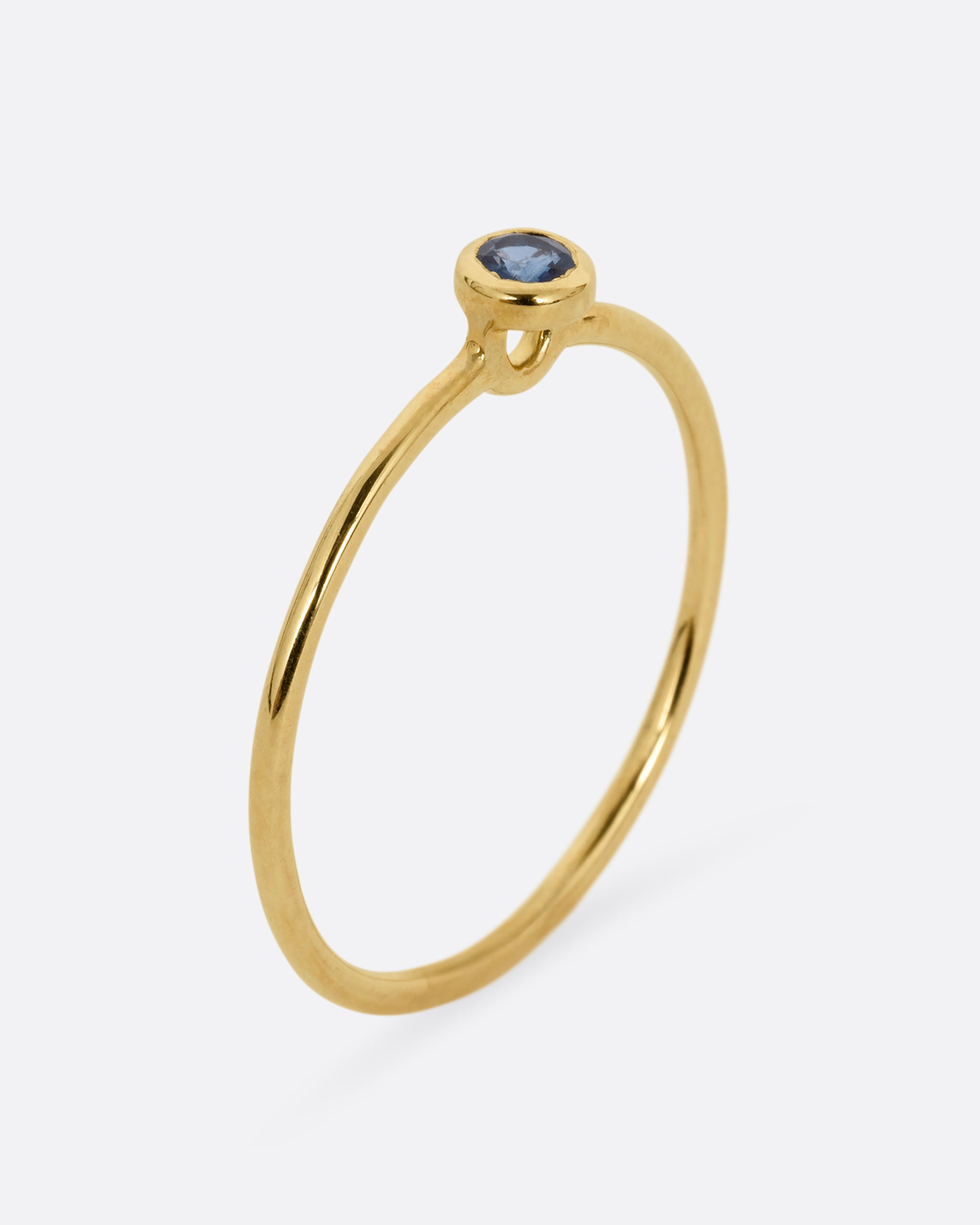 A yellow gold ring with a round sapphire, shown standing up from the front.