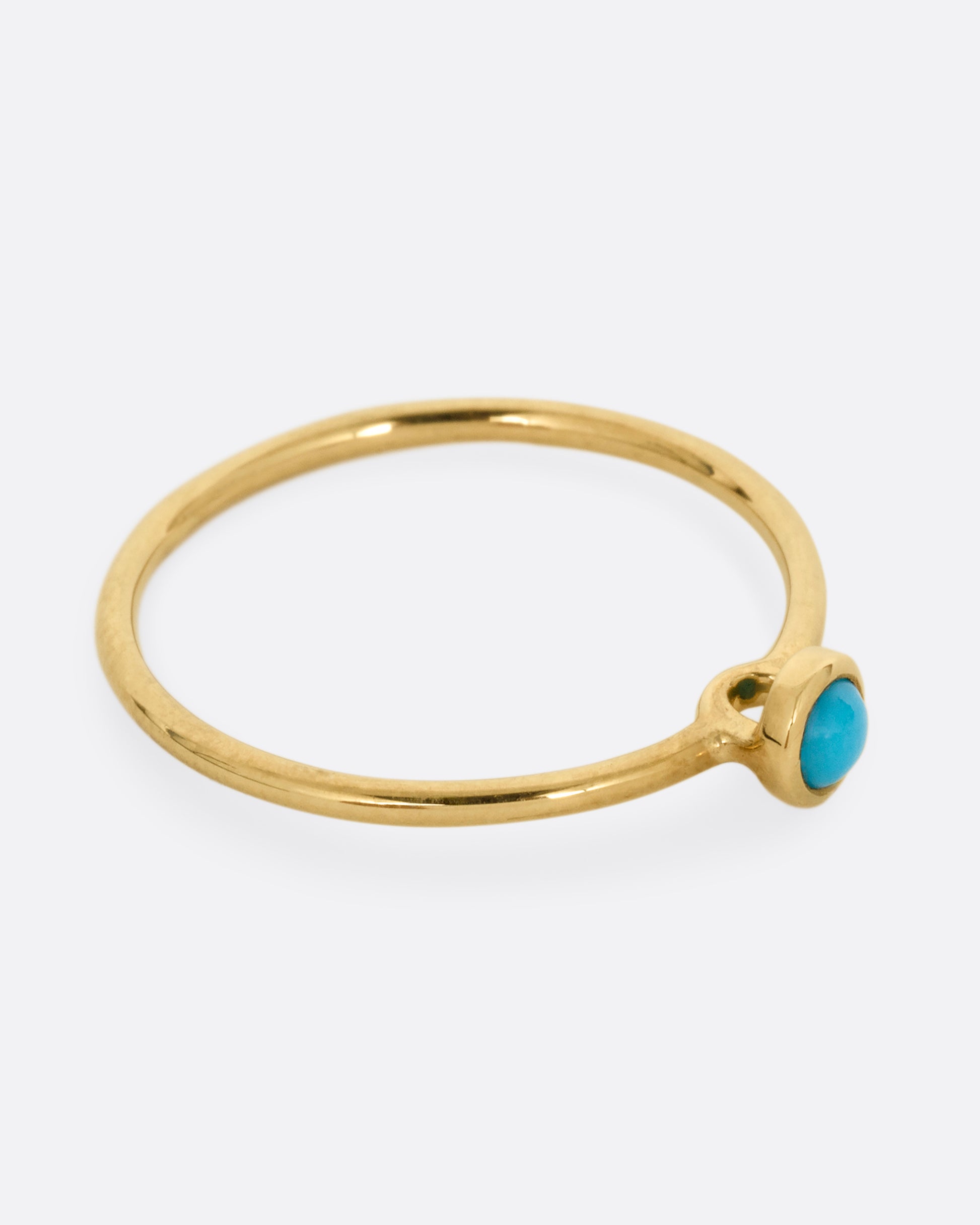 A yellow gold ring with a round turquoise. Shown from the side.