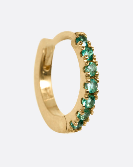A yellow gold hinged hoop earring with pavé emeralds, shown from the side.