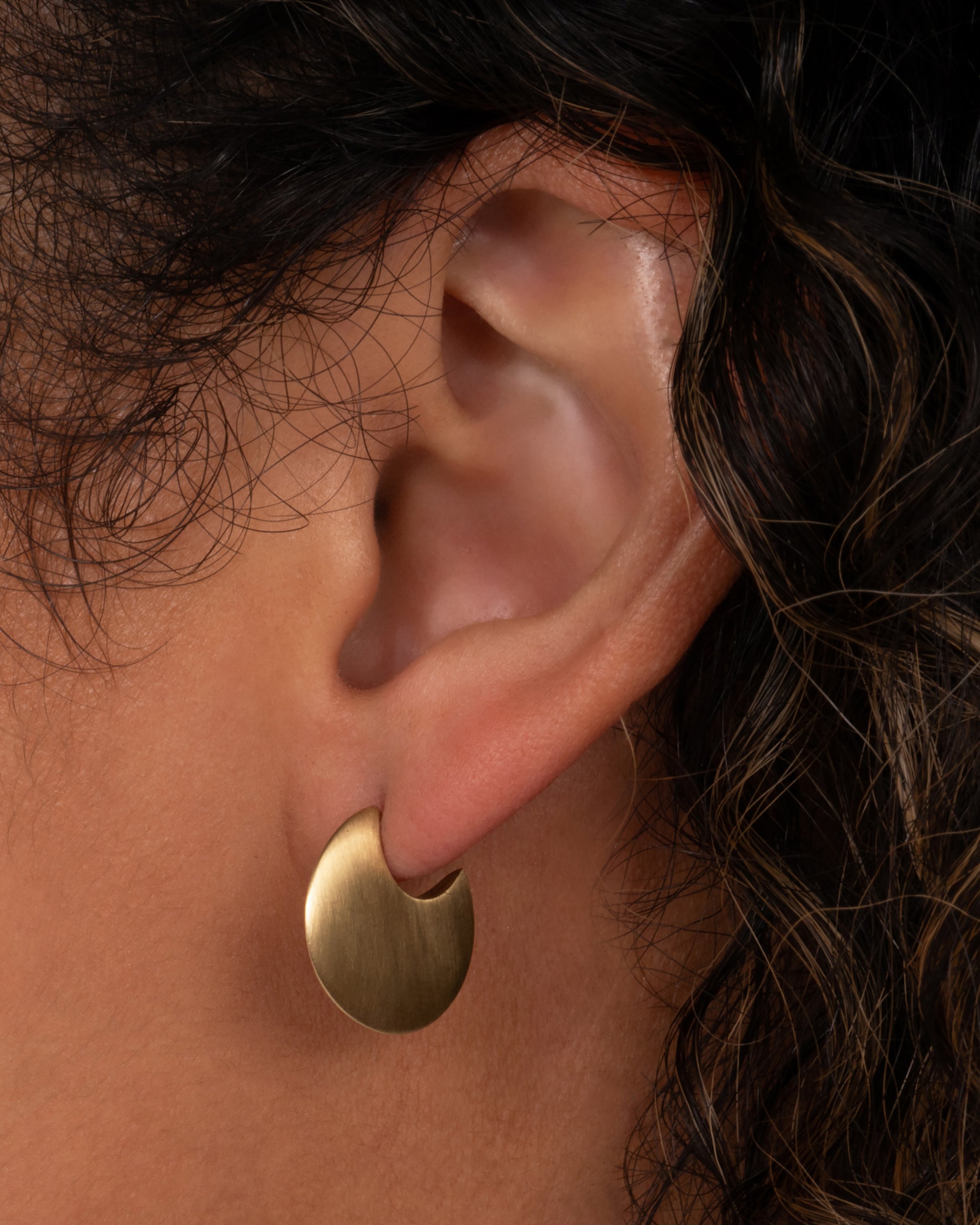 A yellow gold huggie hoop earring shown worn in an ear.