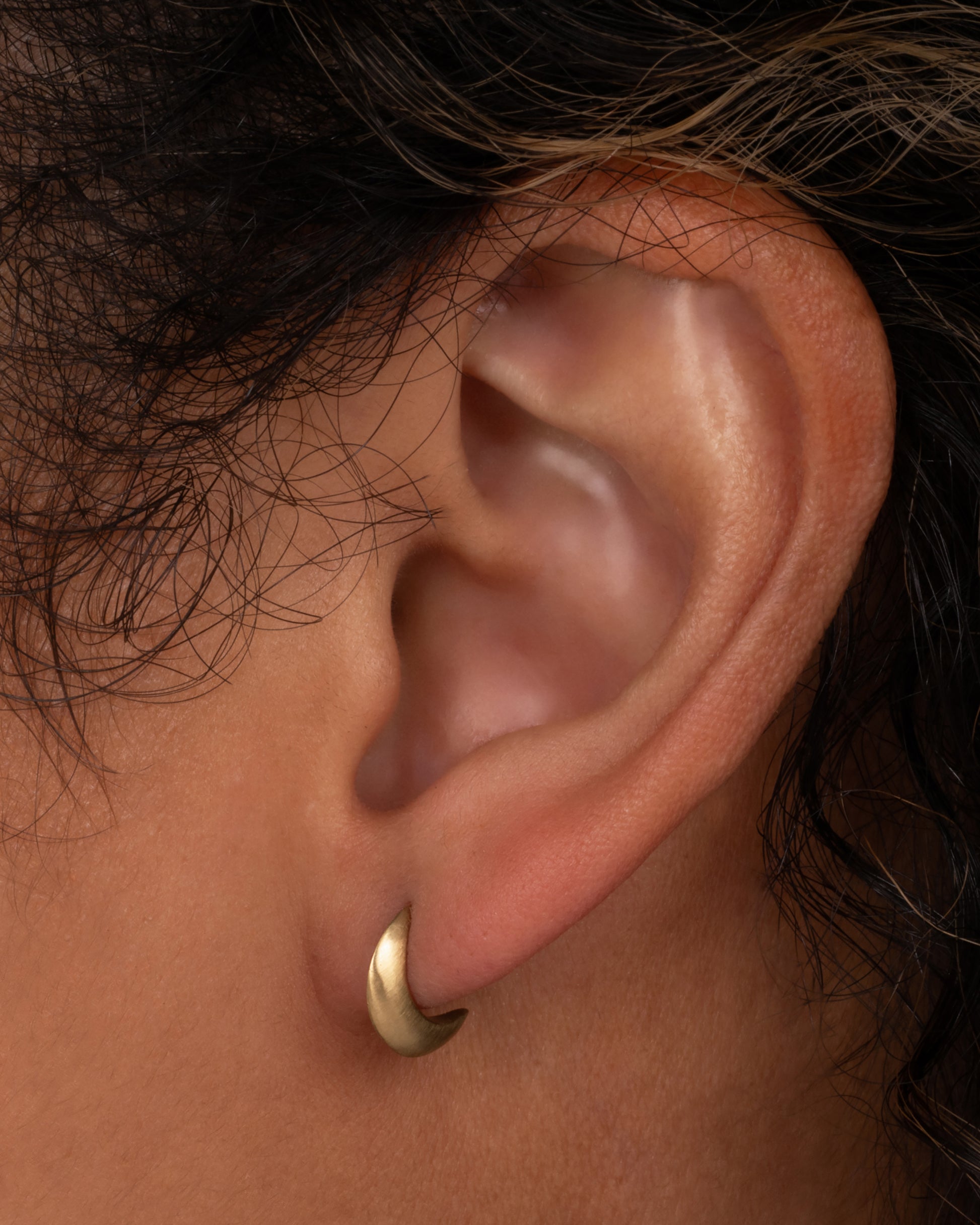 A pair of yellow gold crescent moon shaped earrings with stud backs. Shown worn in an ear.