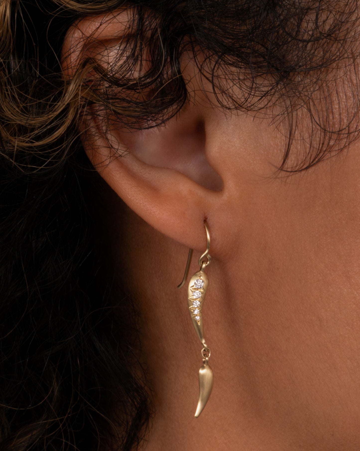 A yellow gold earring with two dangles- one with diamonds, shown on an ear.