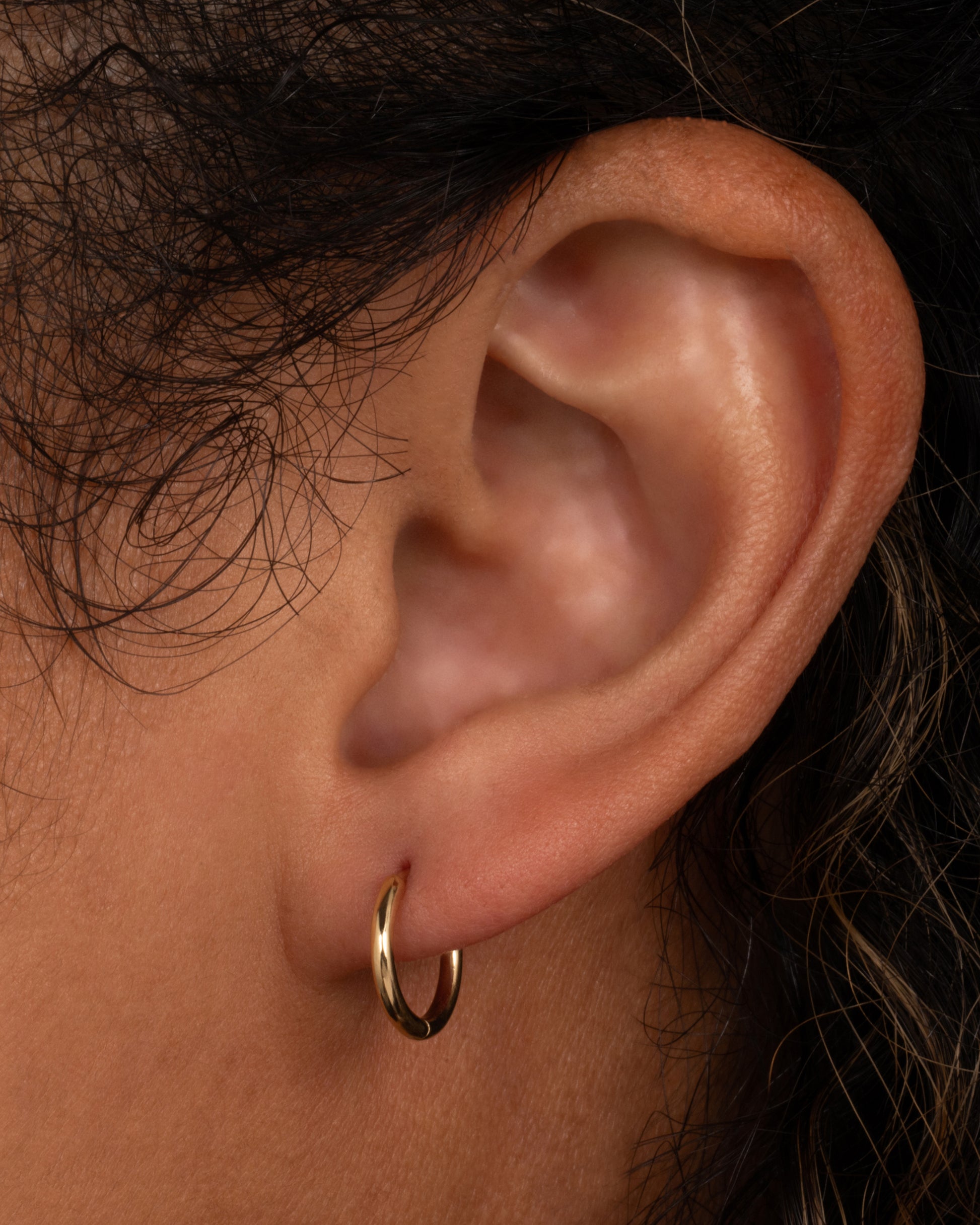 A yellow gold hoop earring with a hinged clicker clasp, shown on a person.