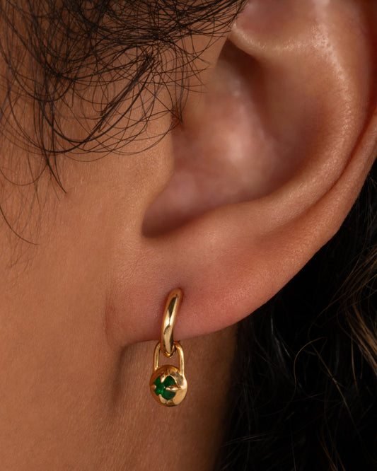 A yellow gold hoop earring with an emerald charm, shown on an ear.