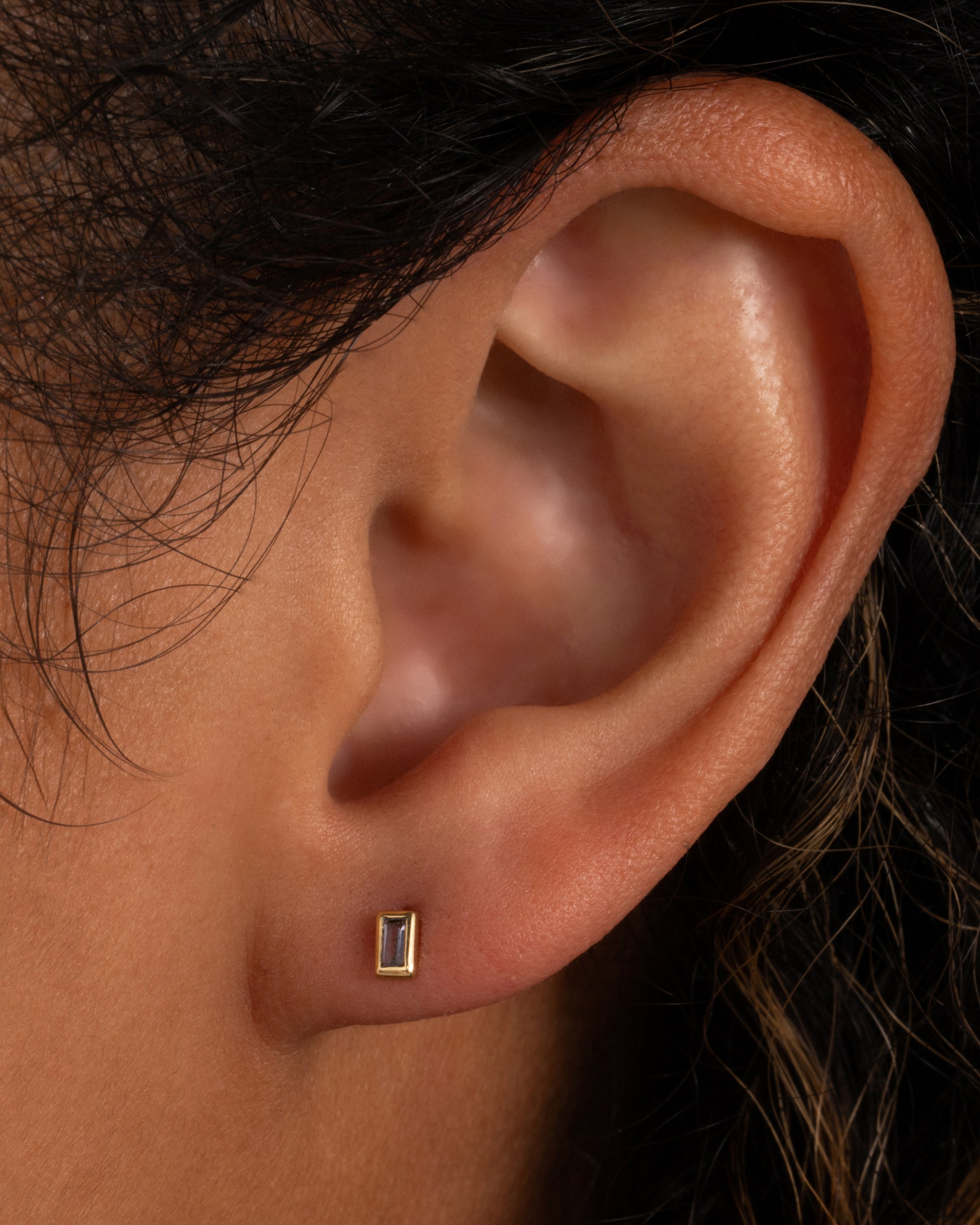 A yellow gold stud earring with a baguette cut tanzanite. Shown in an ear.