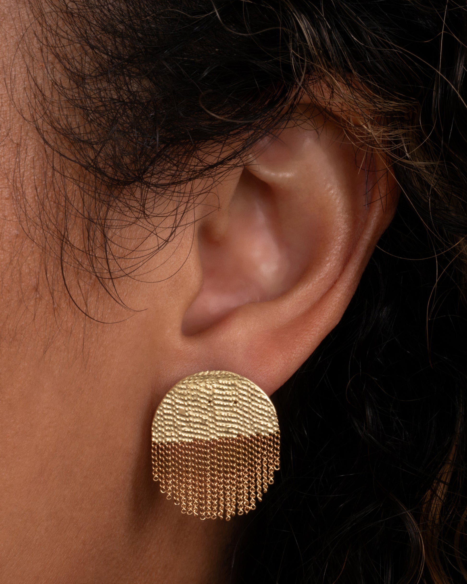 A yellow gold circular stud back earring that's half solid and half fringe chain. Shown in an ear.