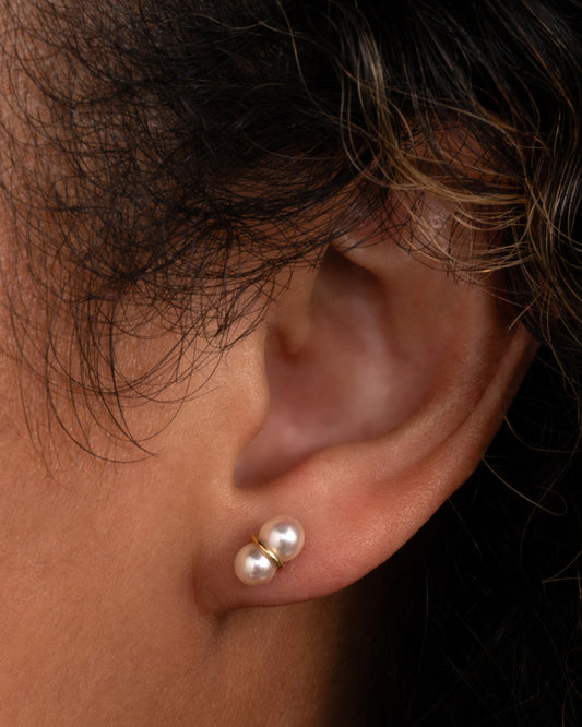 A pearl earring with a gold loop around the middle, shown in an ear.