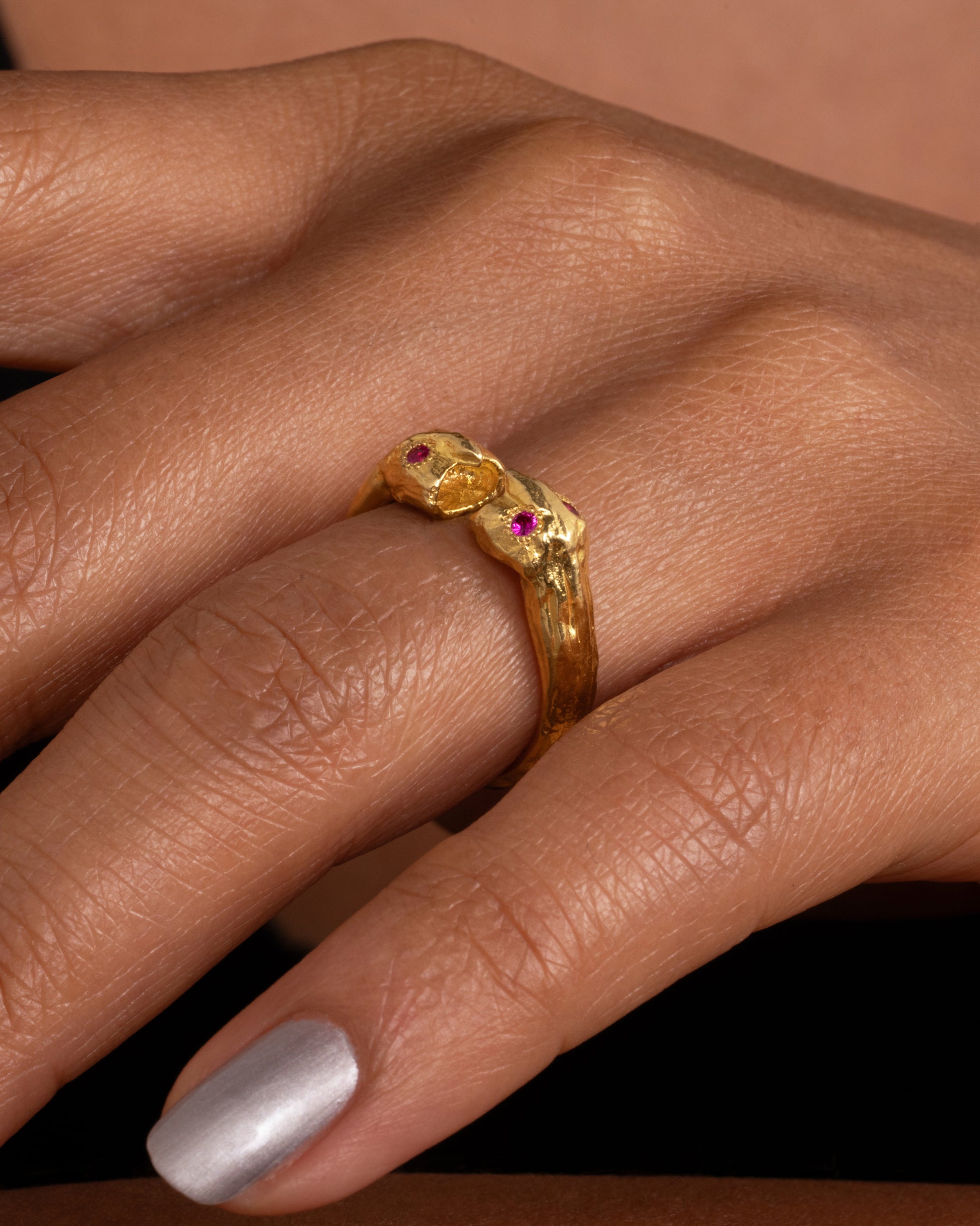Yellow gold ring with two faces with ruby eyes, shown on a hand.