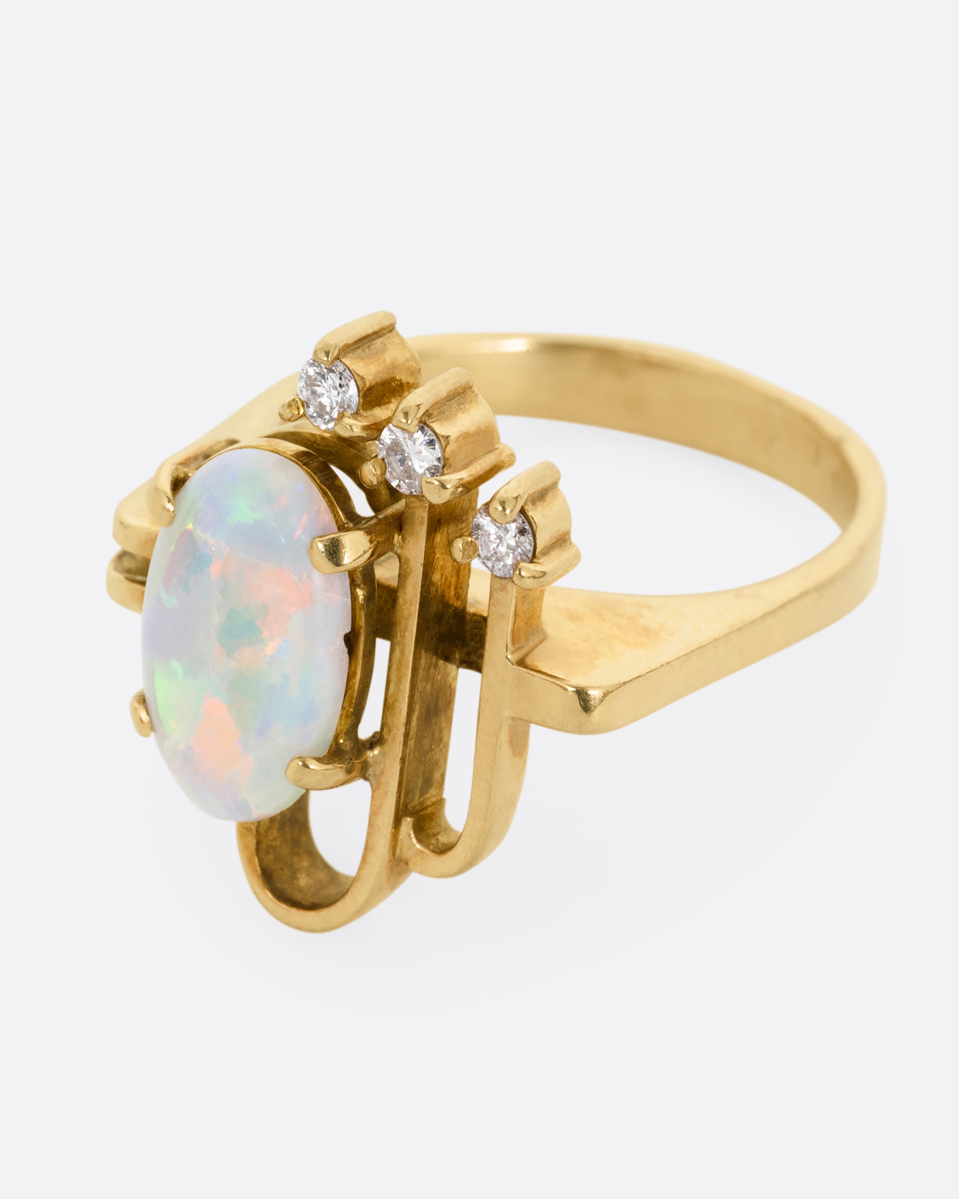 A yellow gold ring with a trio of diamonds, two Deco- inspired arches, and a prong set opal. Shown from the side.