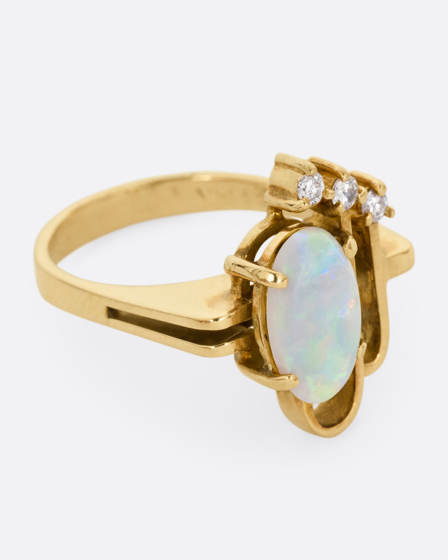 A yellow gold ring with a trio of diamonds, two Deco- inspired arches, and a prong set opal. Shown from the side.