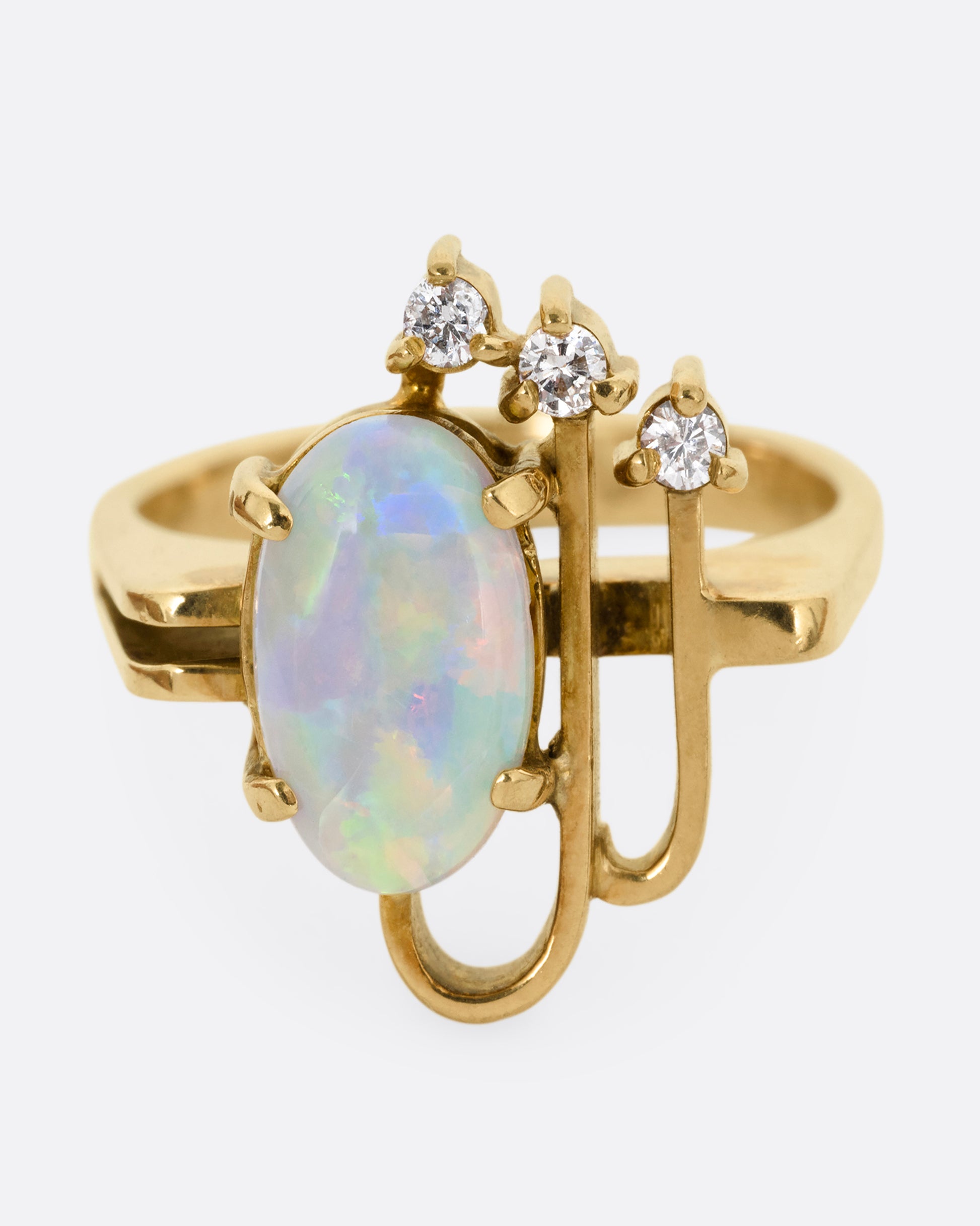 A yellow gold ring with a trio of diamonds, two Deco- inspired arches, and a prong set opal. Shown from the front.