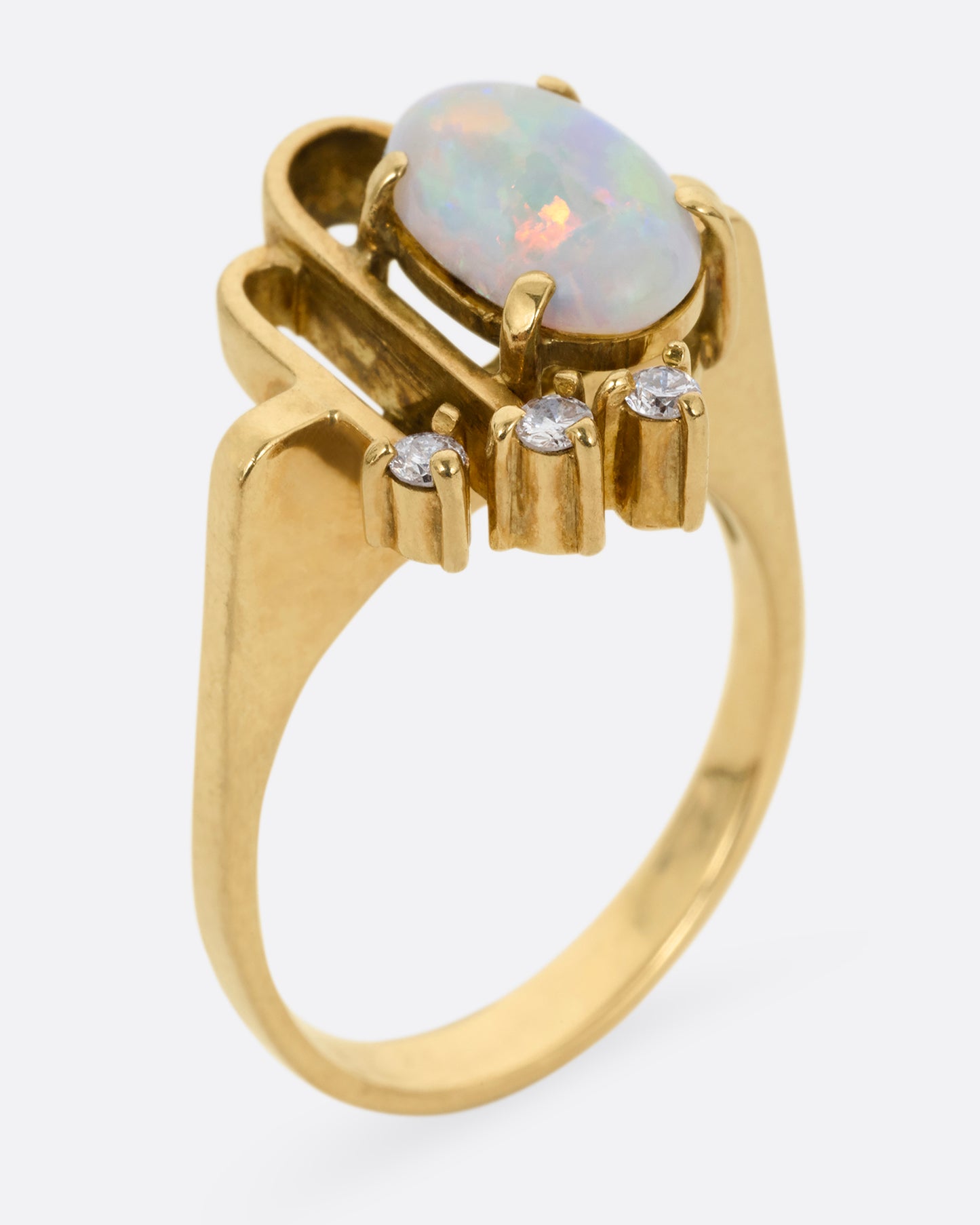 A yellow gold ring with a trio of diamonds, two Deco- inspired arches, and a prong set opal. Shown standing up from the side.