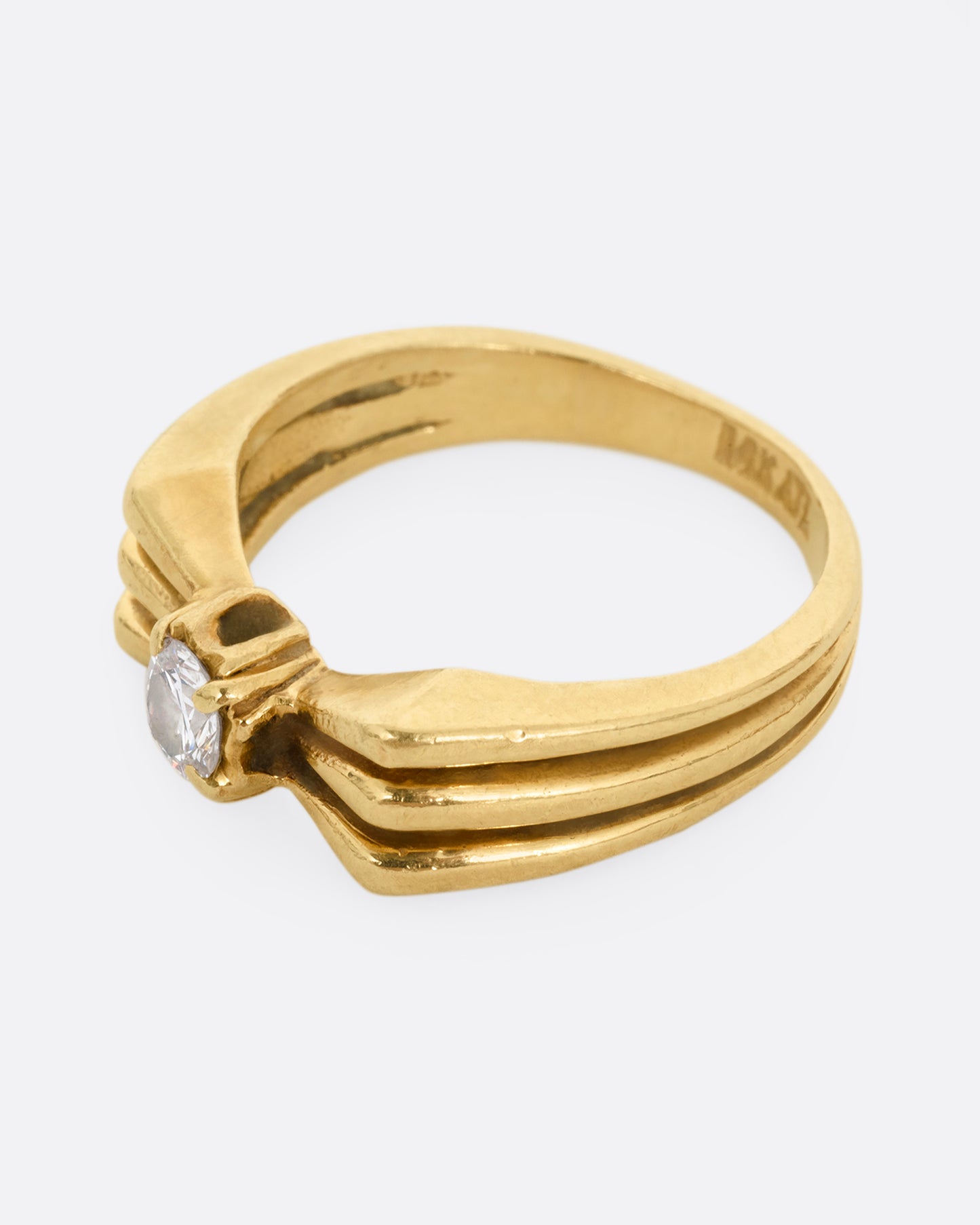 A yellow gold ring with a stacked silhouette and angular shoulders and a prong set diamond at the center. Shown from the side. 