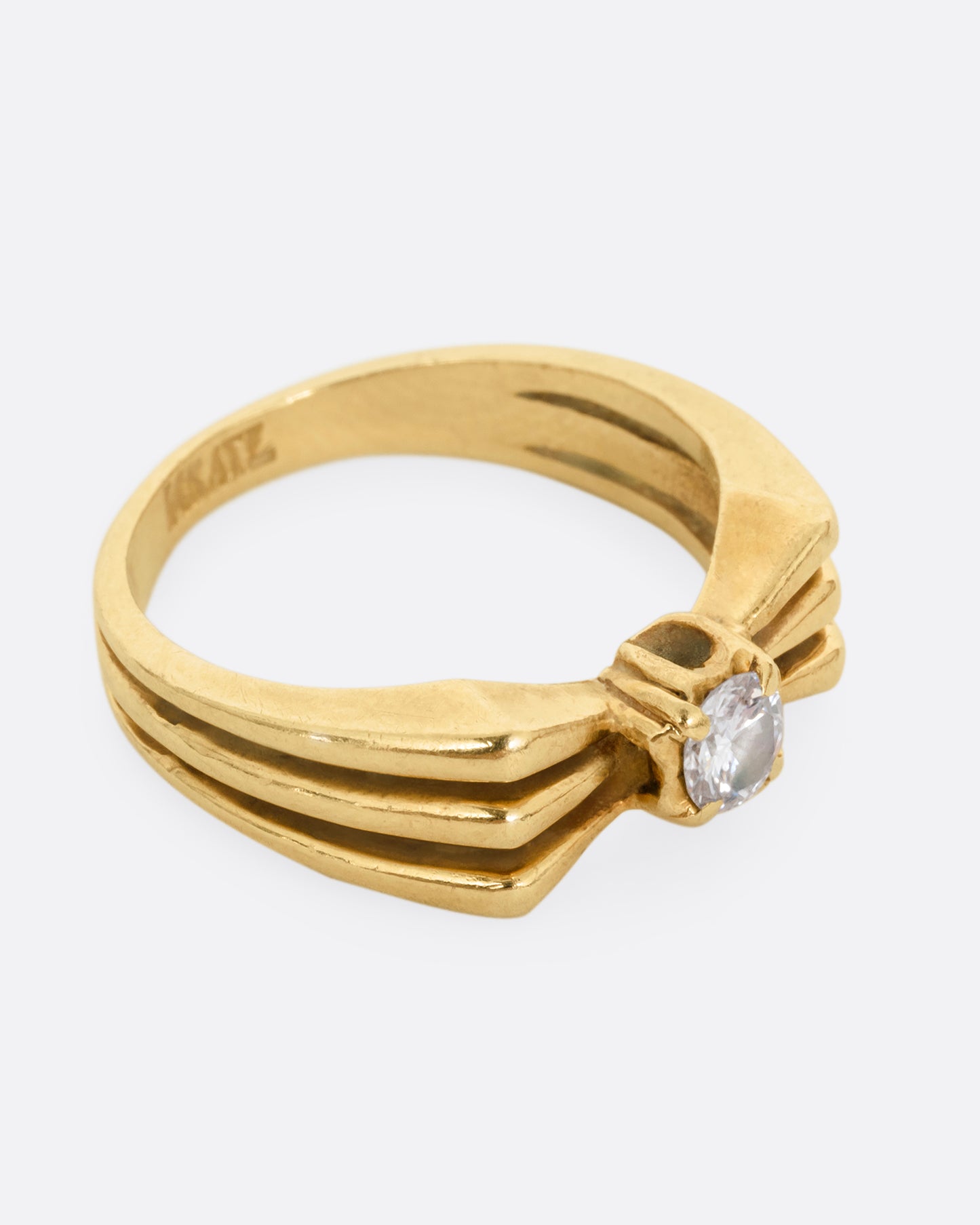 A yellow gold ring with a stacked silhouette and angular shoulders and a prong set diamond at the center. Shown from the side. 