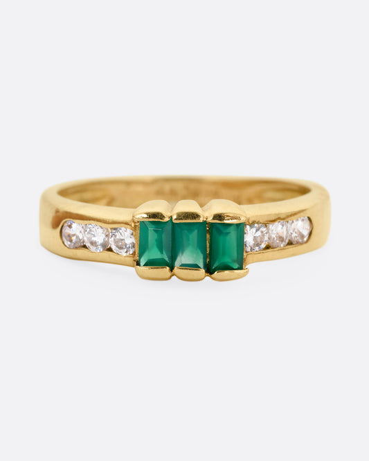 A yellow gold ring with six white diamonds and three emerald baguettes, shown from the front.