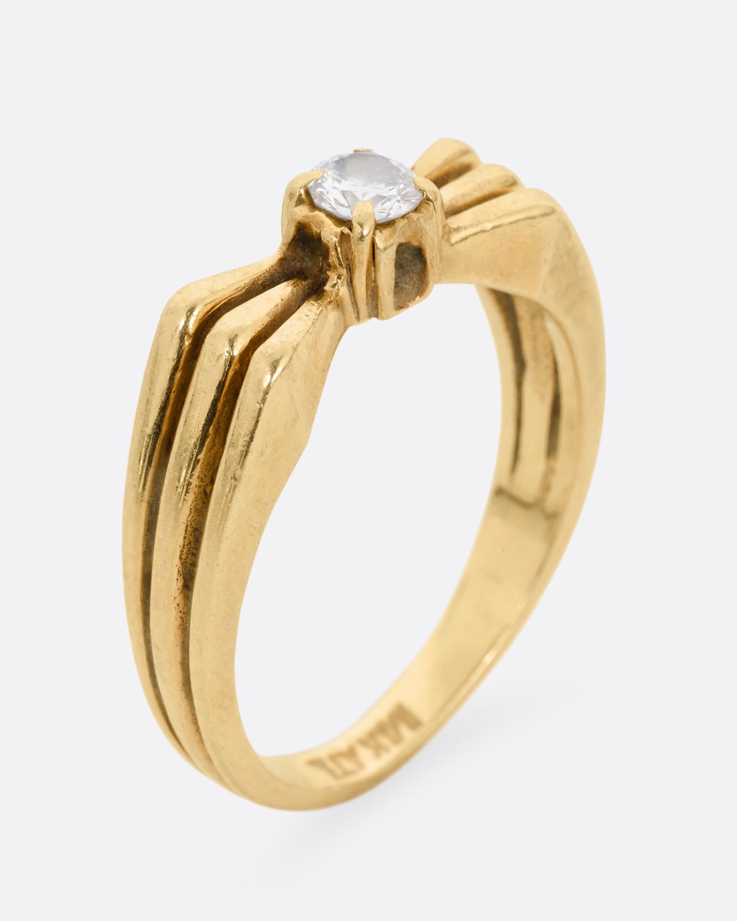 A yellow gold ring with a stacked silhouette and angular shoulders and a prong set diamond at the center. Shown standing up from the side. 