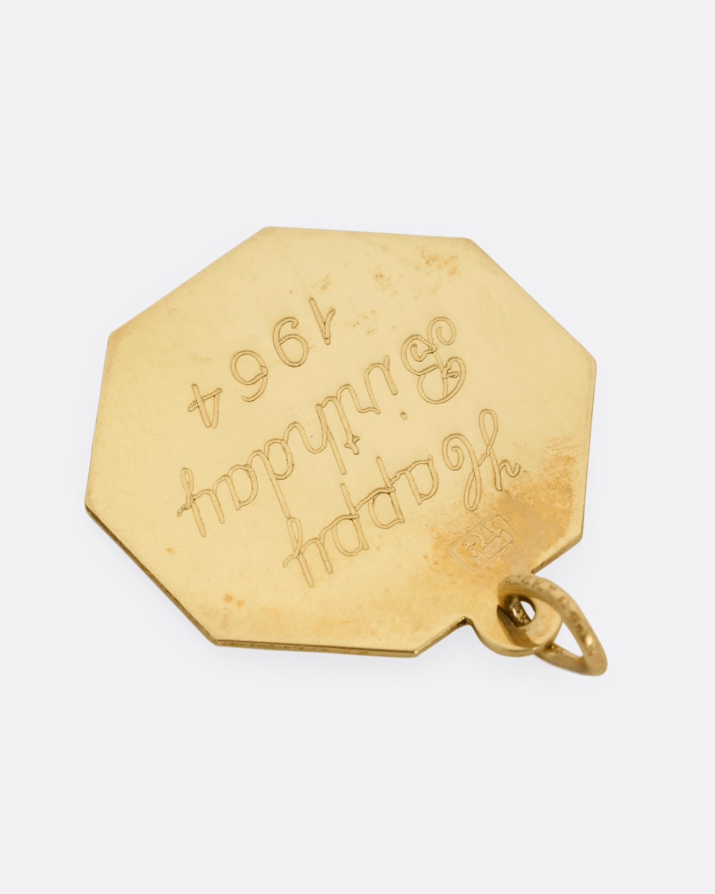 A yellow gold octagon shaped pendant with an engraved 'Happy Birthday 1964' on the back. Shown from the back.