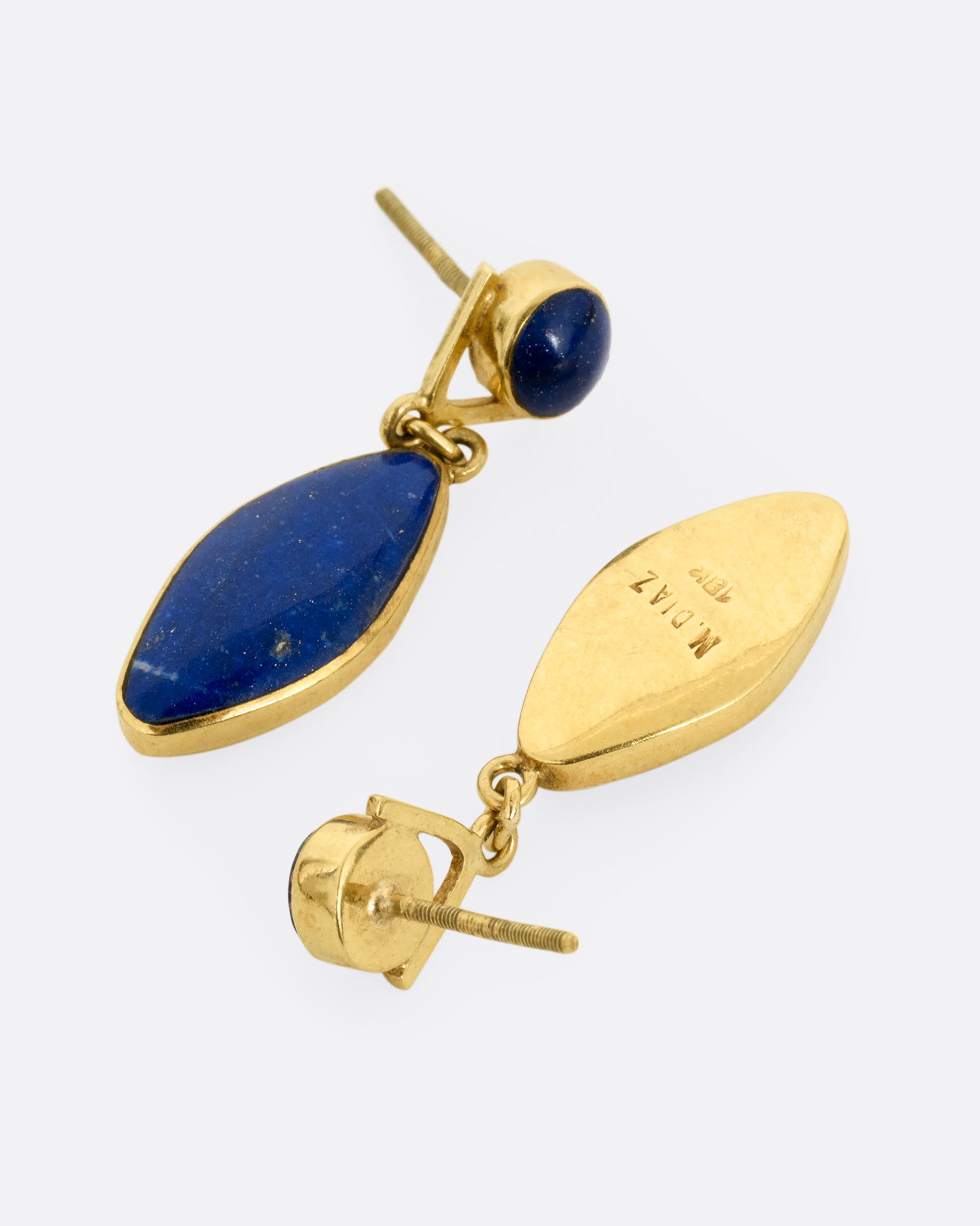 A pair of yellow gold lapis drop earrings with round lapis stud tops. Shown lying on their sides, one from the front, the other from the back open.