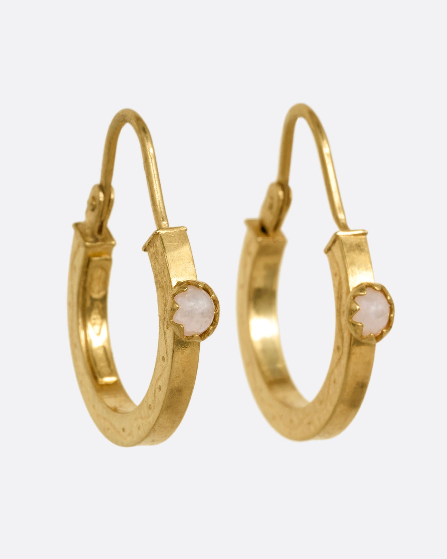 A pair of yellow gold hoop earrings, each with a pearl, shown from the side.