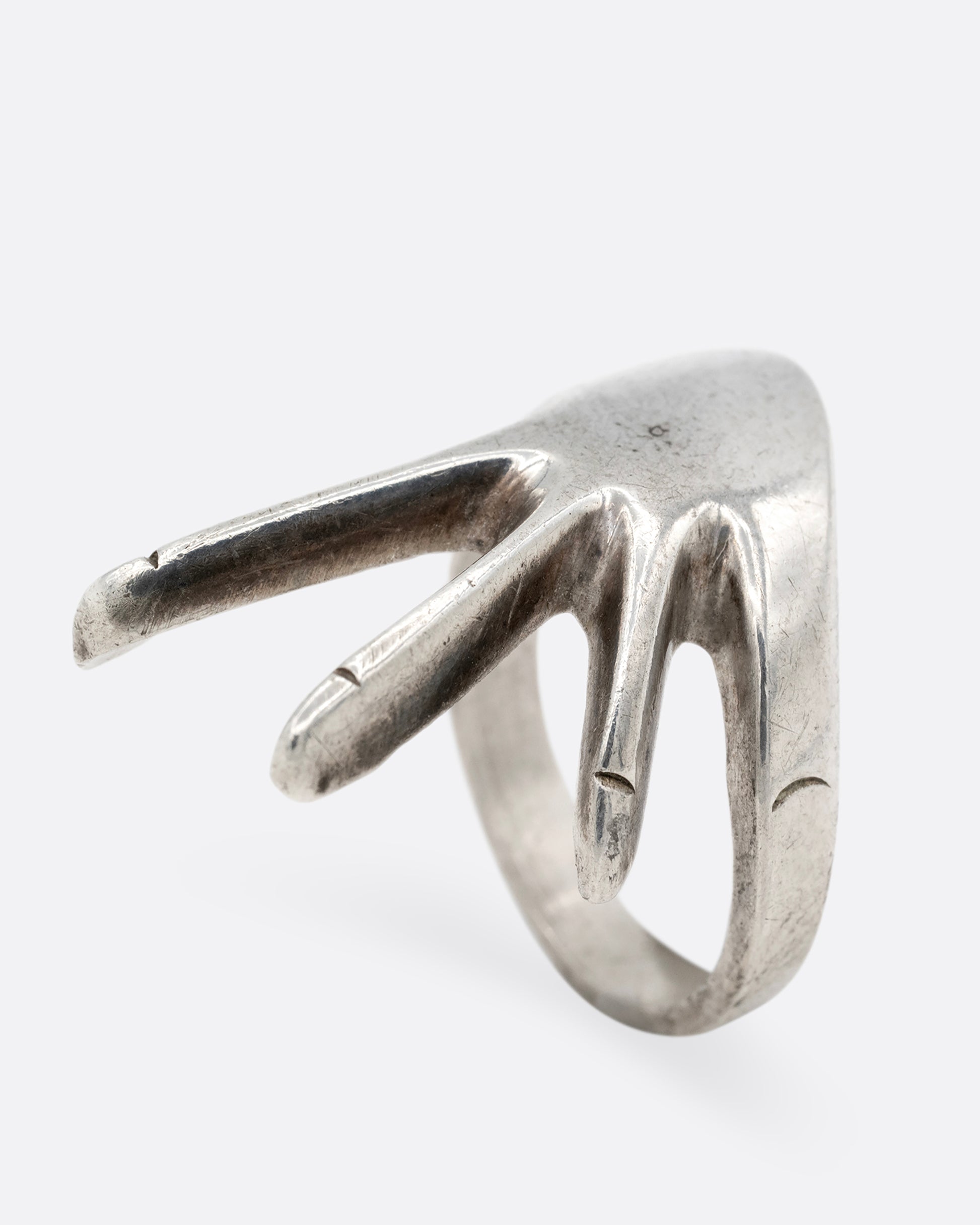 A silver hand shaped ring with long fingers, shown standing up from the side.