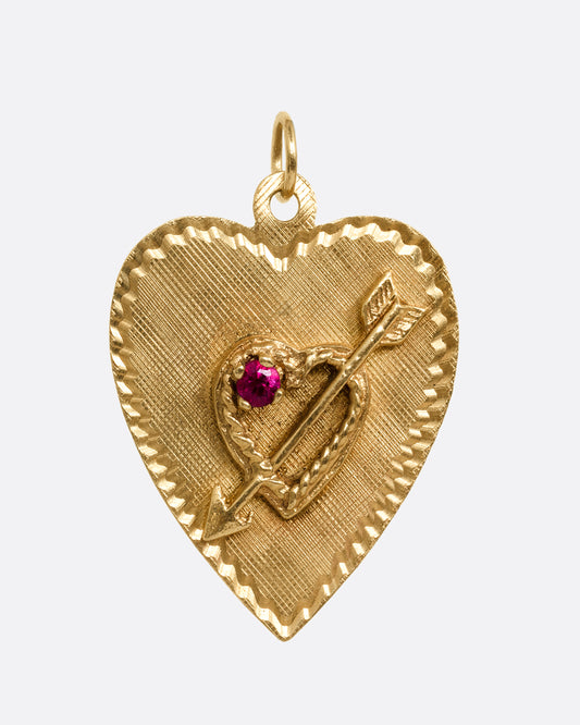 A yellow gold heart shaped pendant with a ruby and small arrow- stricken heart at the center. Shown from the front.