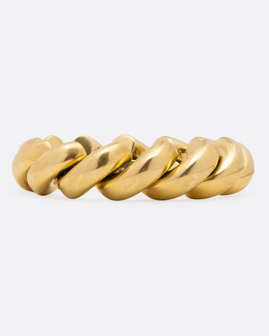 A chunky gold curved chain-link bangle bracelet with a polished finish, displayed on a clean light gray background.