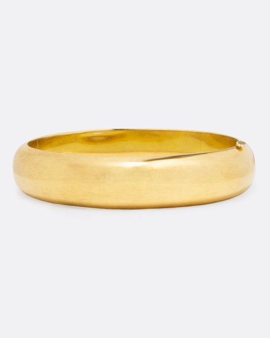 A wide yellow gold oval hinged bangle shown from the front on a light background.