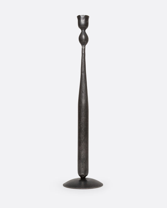 A tall, slender iron candlestick holder with  a flared circular base, shown from the front.