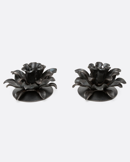 A pair of iron candle holders shaped like stylized flowers, shown from the front.