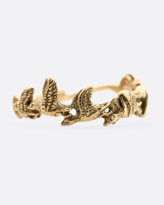 A yellow gold ring with birds flying around the majority of the band. Shown from the front.
