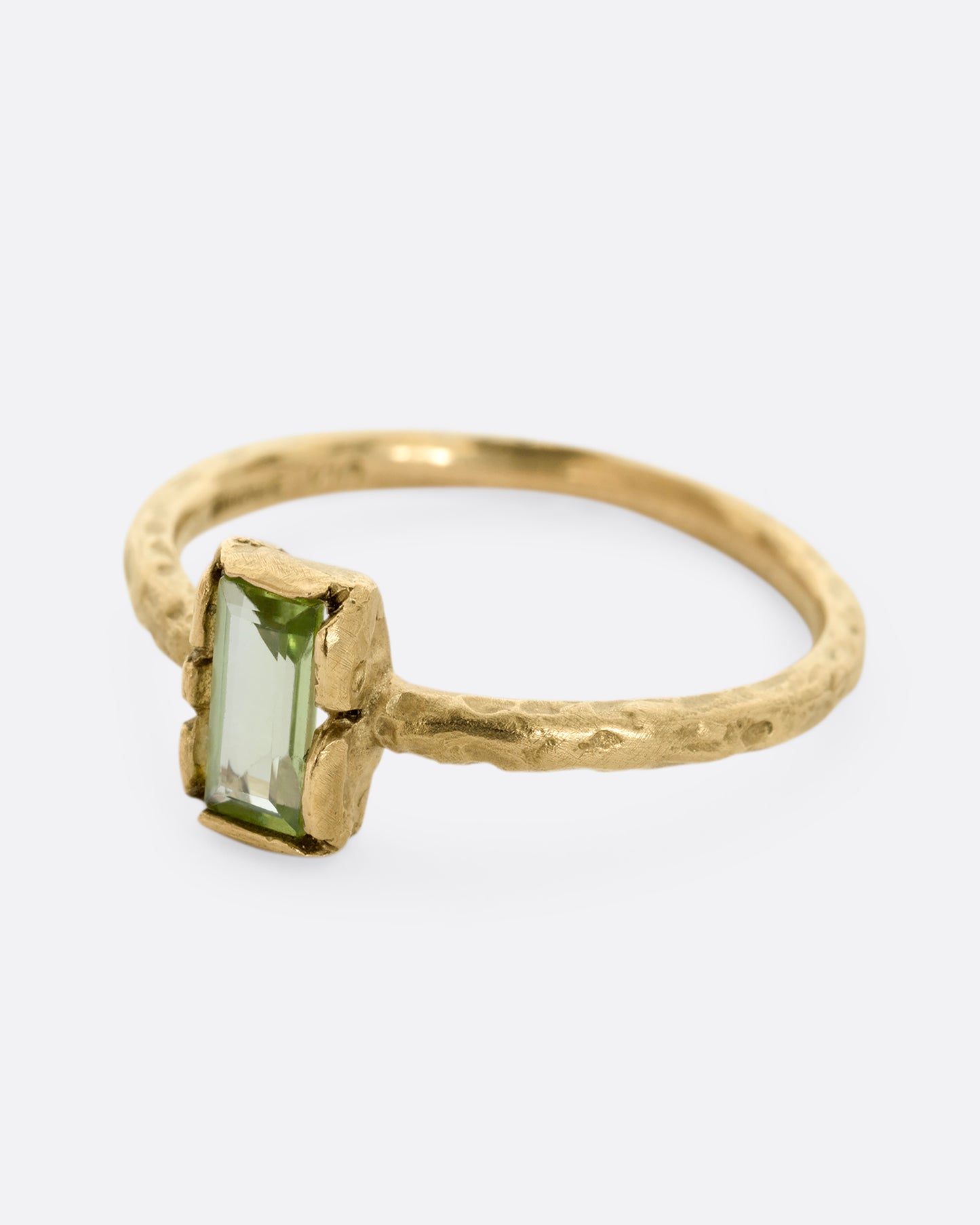 A textured yellow gold ring with a rectangular peridot. Shown from the side.